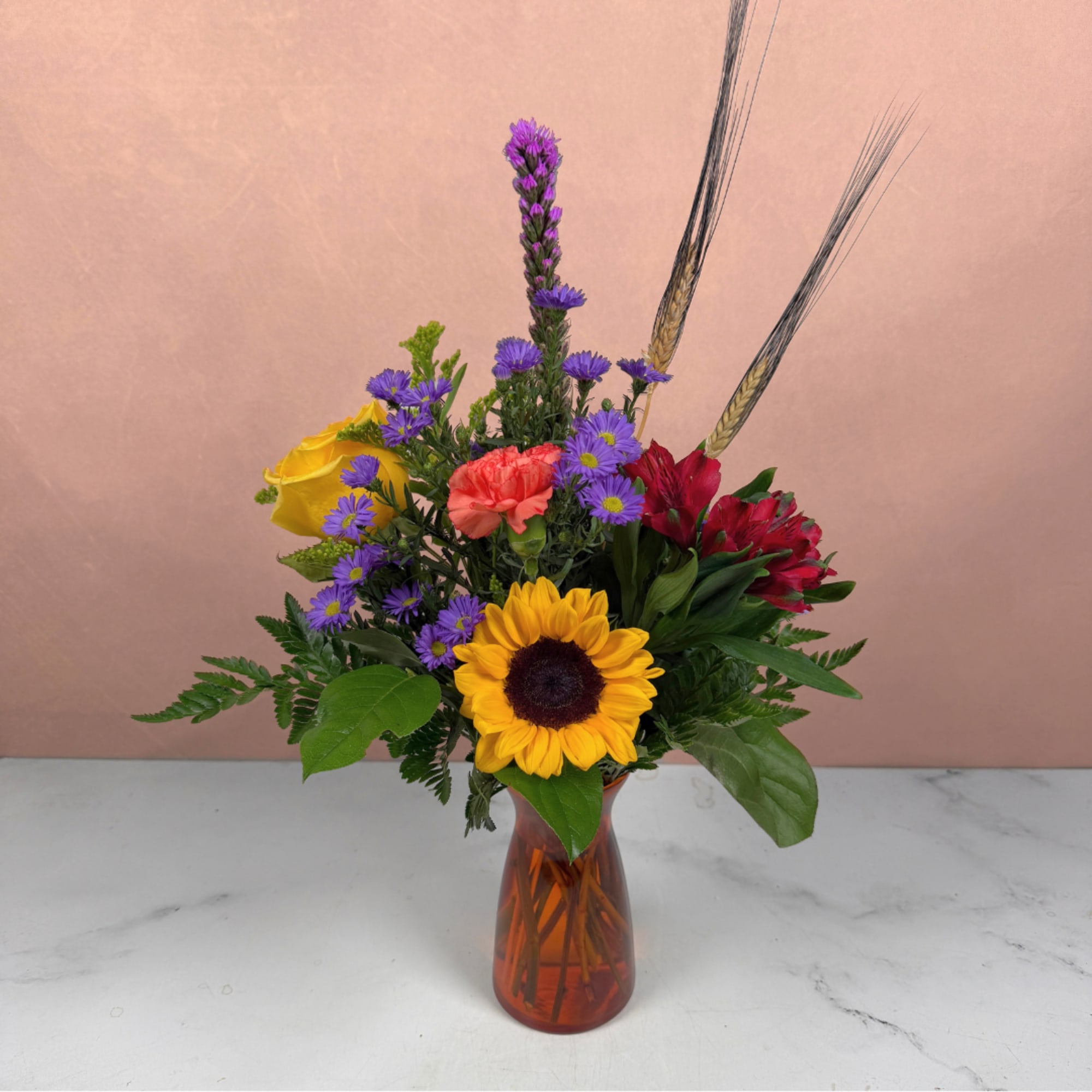 Mixed bouquet in an amber glass vase with a sunflower, roses, and purple daisies