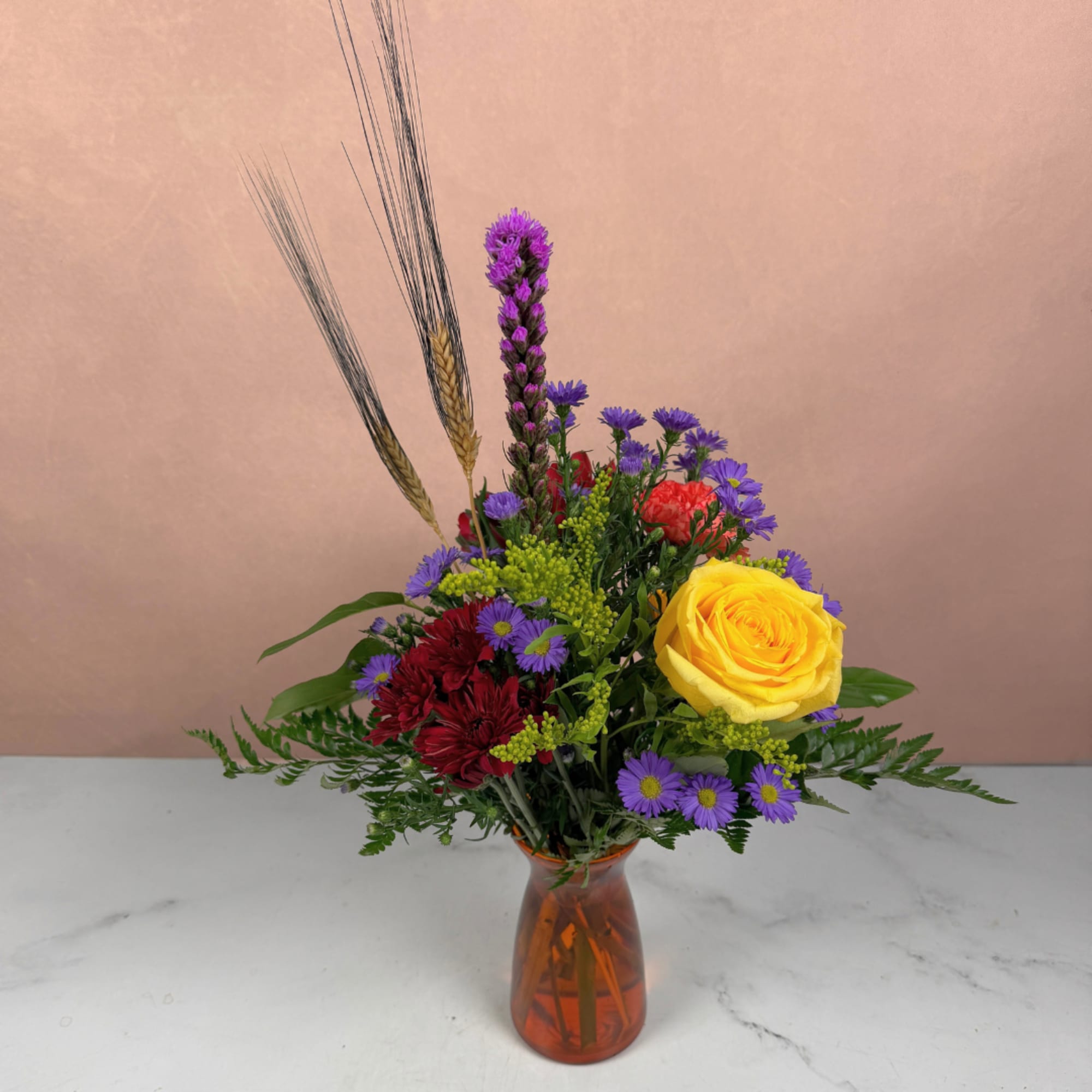 Mixed bouquet in an amber vase with a yellow rose and purple blooms