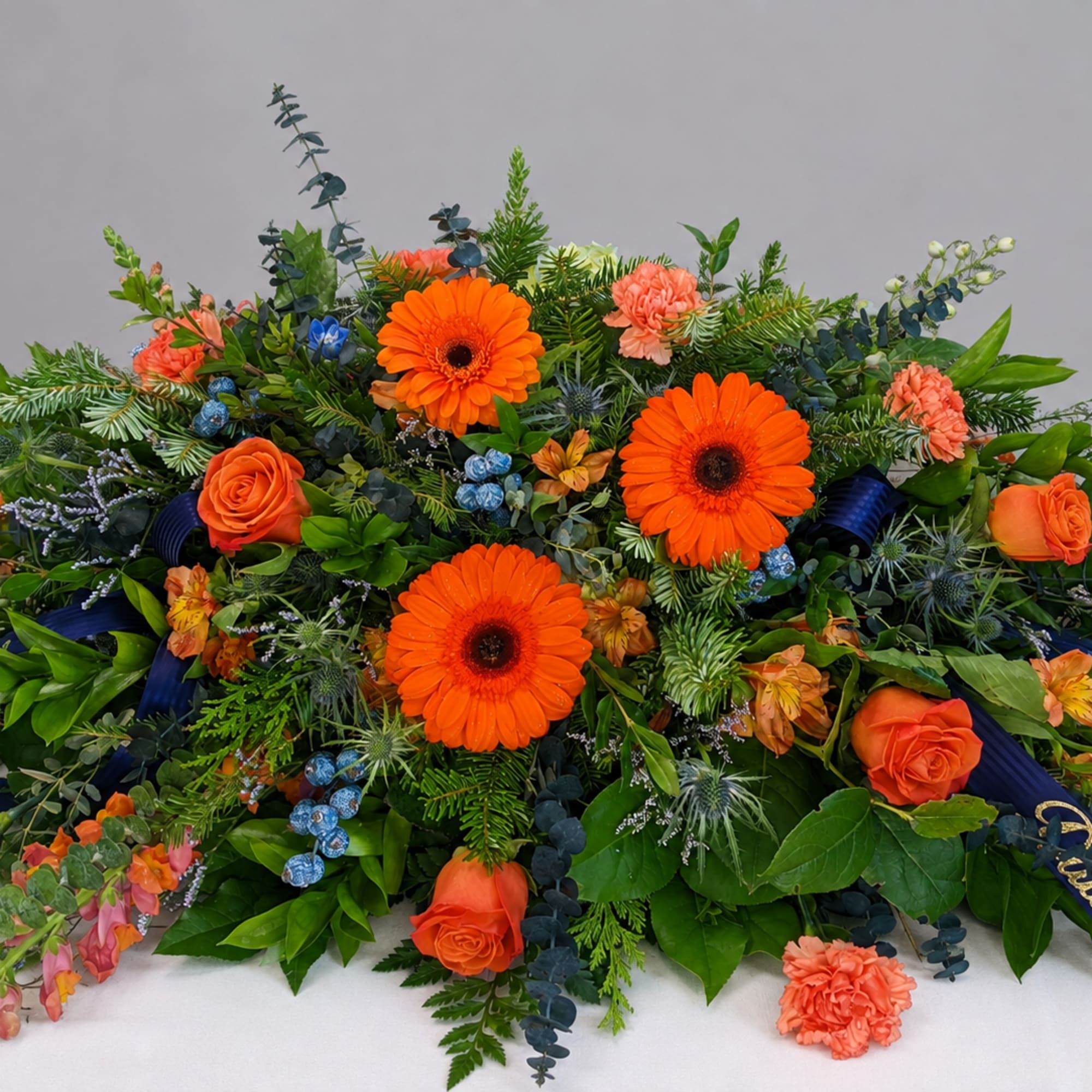 Large orange and coral floral arrangement with blue accents and ribbon
