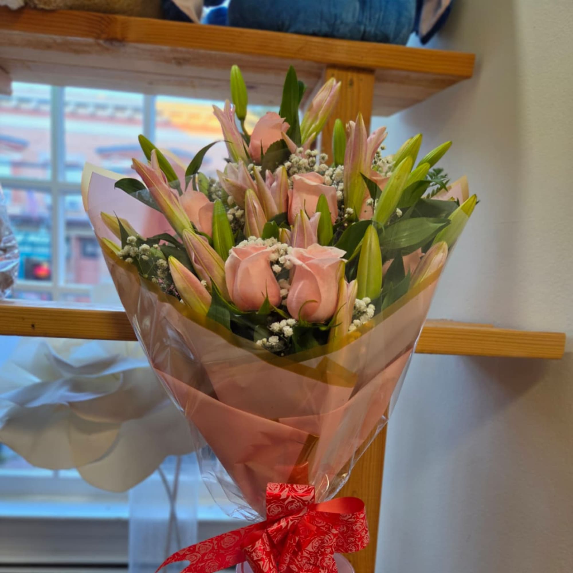 Pink roses and lilies wrapped in pink paper with a red ribbon