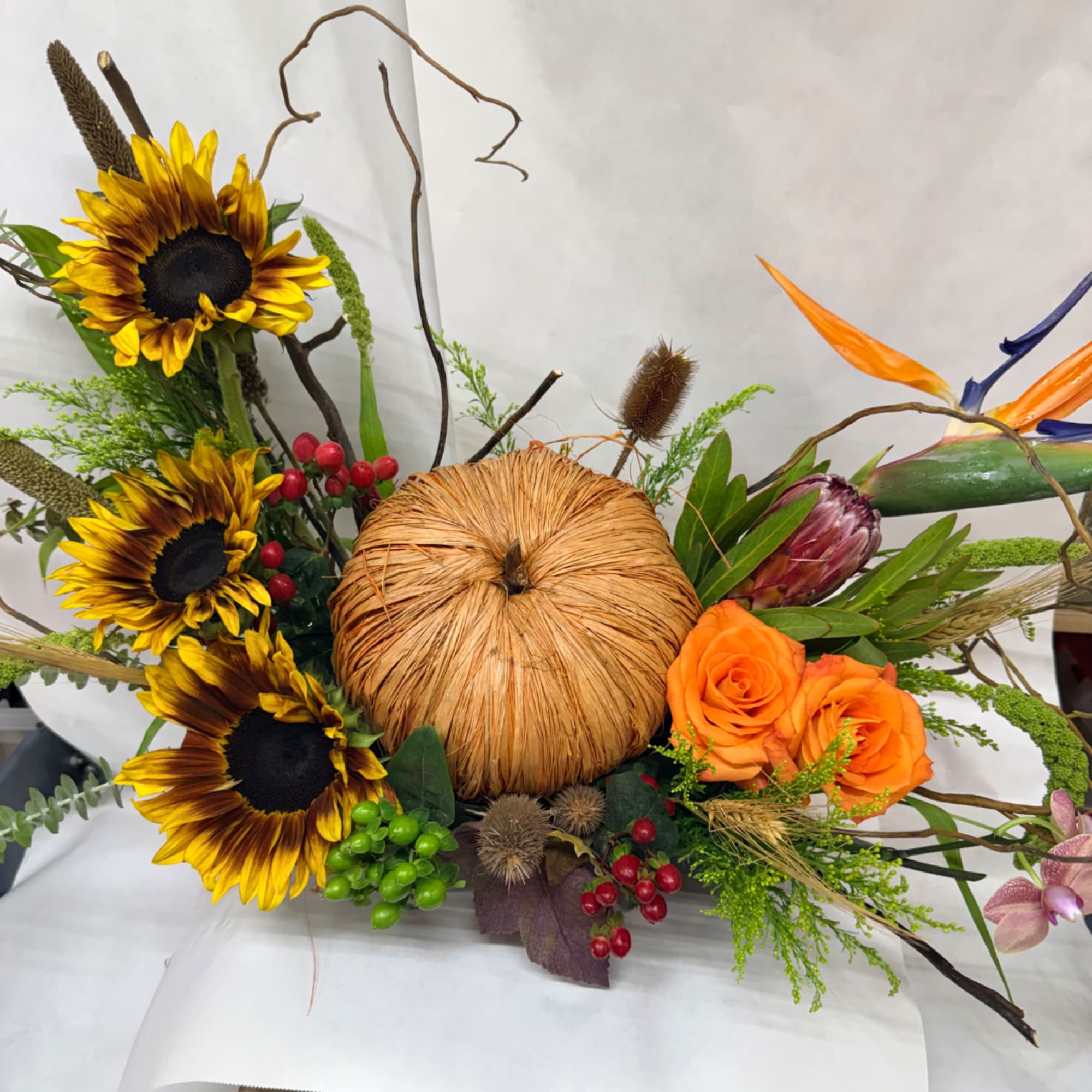 Autumn floral arrangement with sunflowers and orange roses around a pumpkin centerpiece