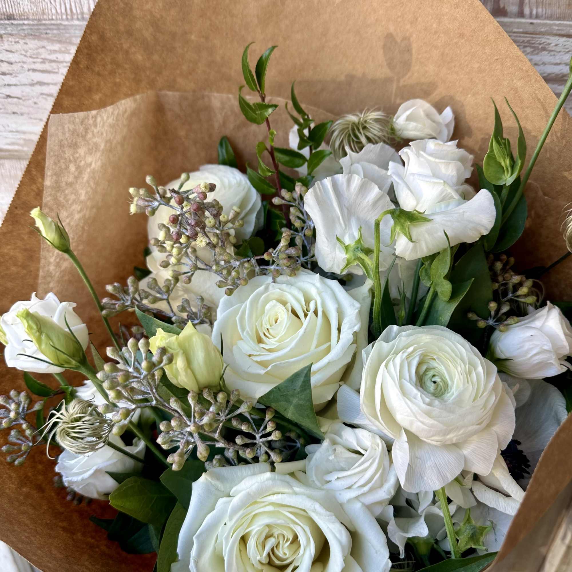 Bouquet of white roses and white ranunculus wrapped in brown paper