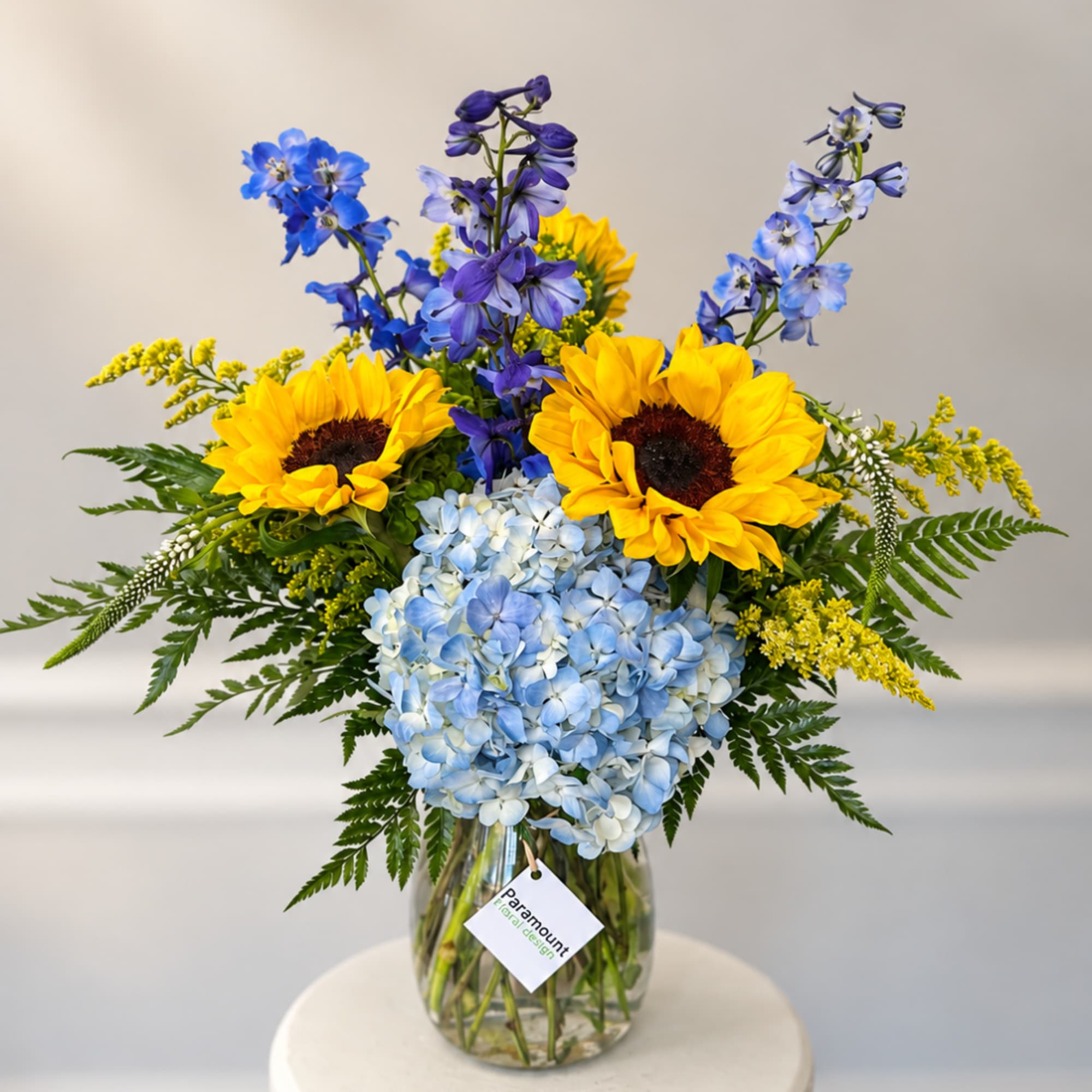 Sunflowers, blue hydrangea, and purple delphinium in a glass vase