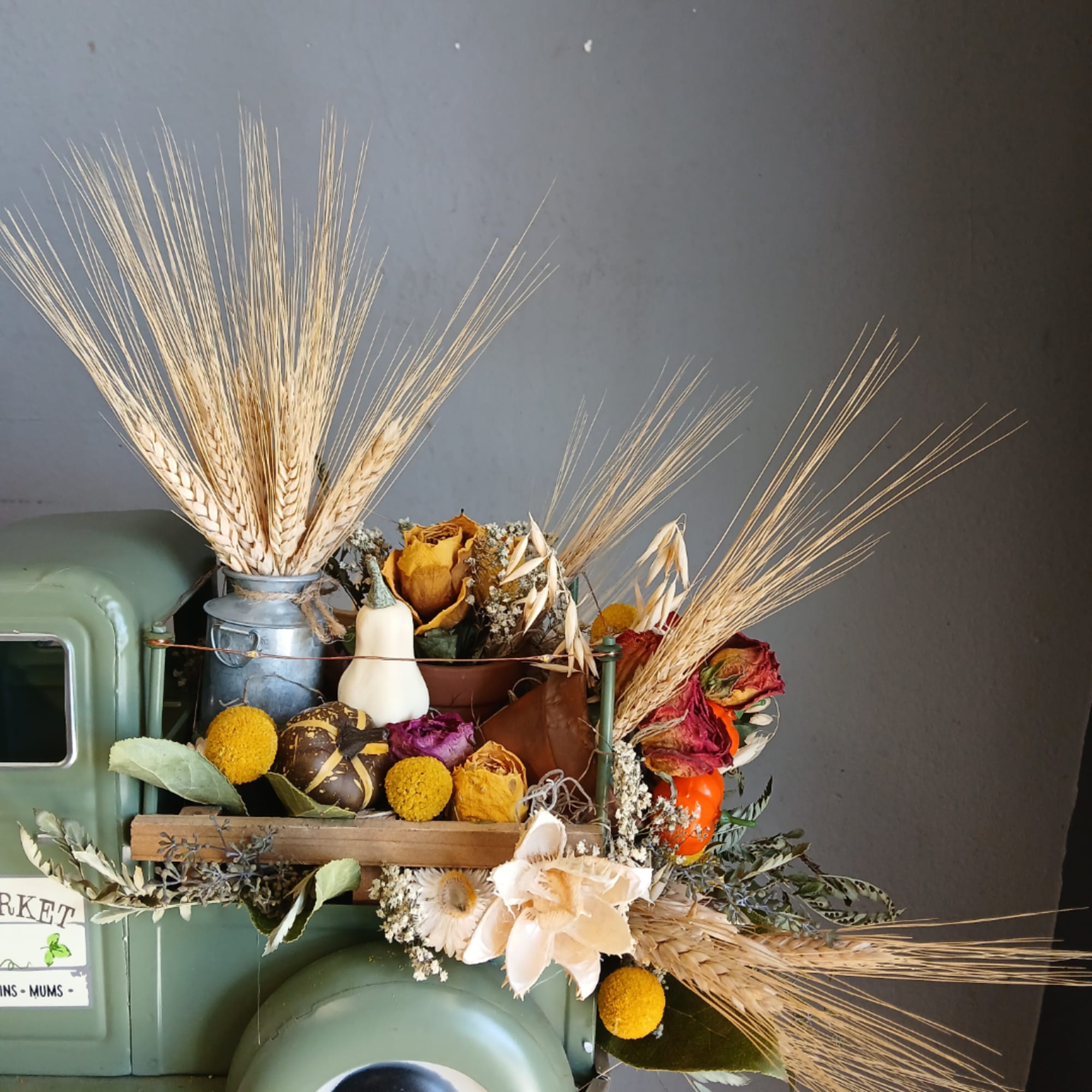 Dried floral arrangement with wheat, roses, and gourds in a rustic container