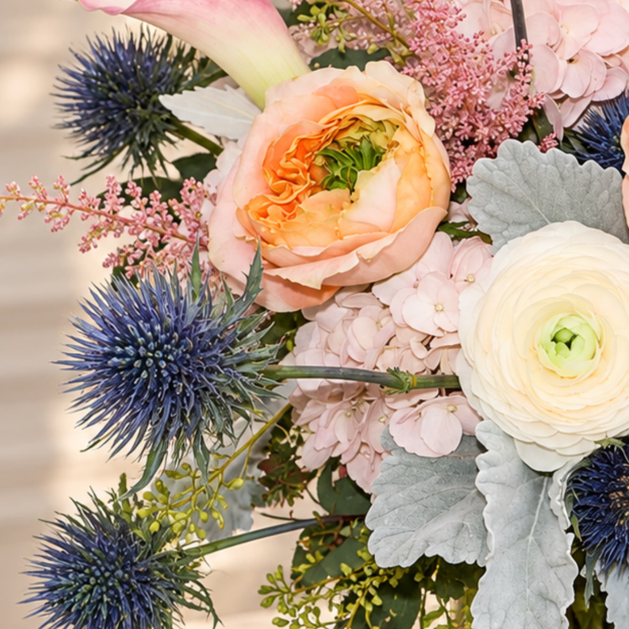 Pastel bouquet with peach and white blooms and blue thistle flowers