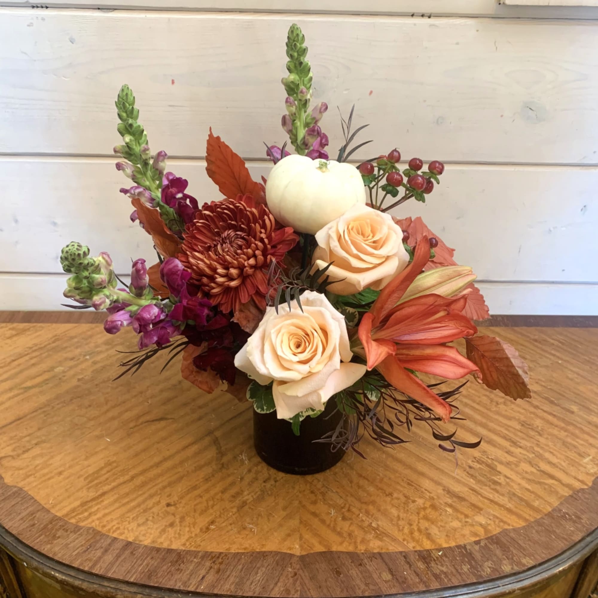 Compact floral arrangement with cream roses, burgundy blooms, and a white pumpkin in a black vase