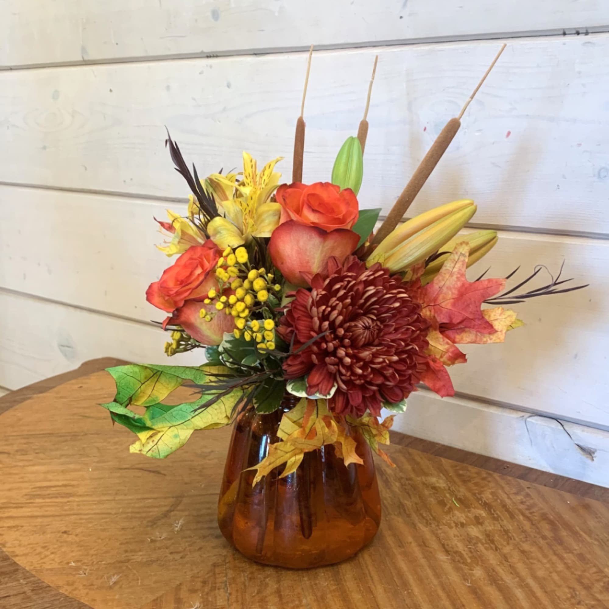 Autumn floral arrangement in an amber glass vase with orange and yellow blooms