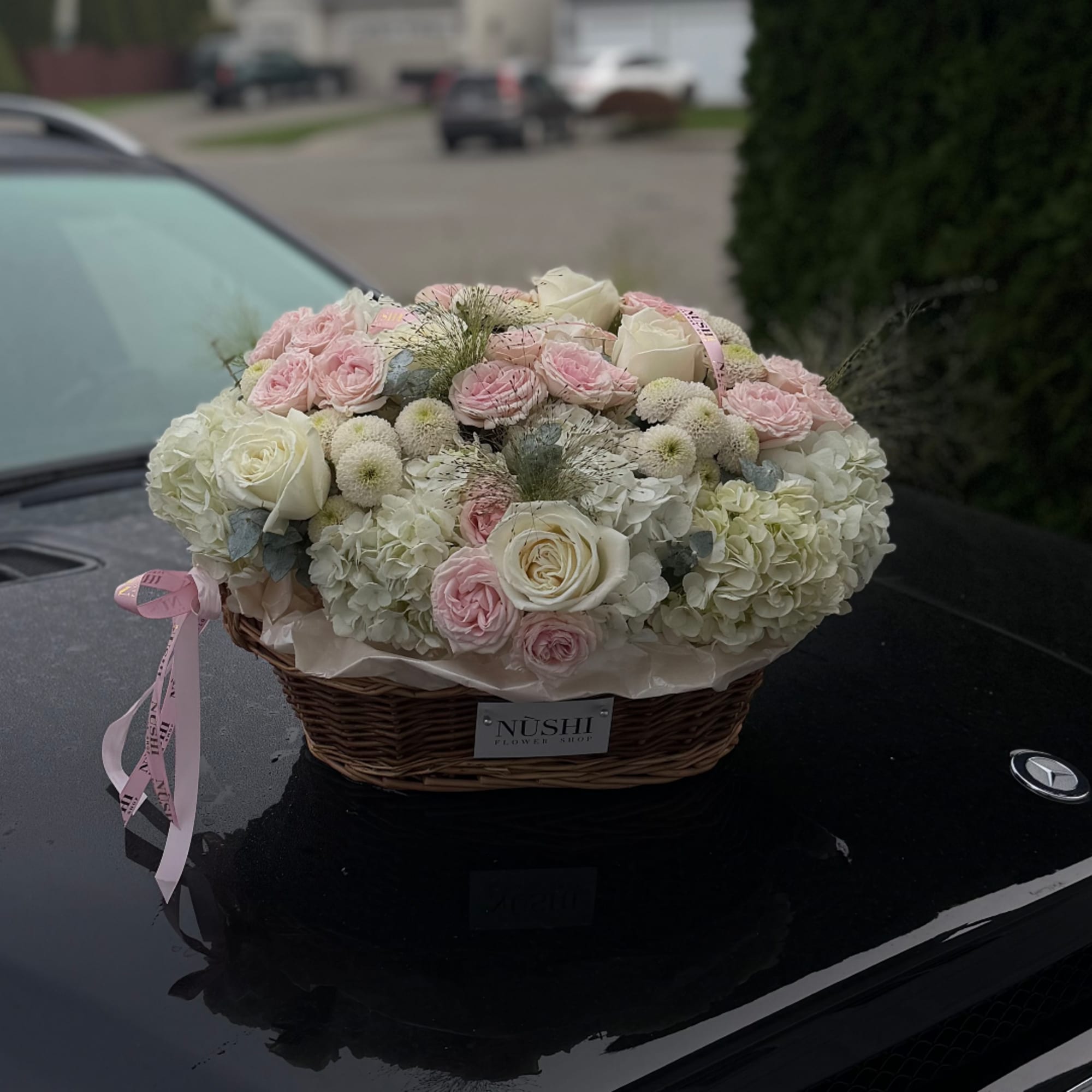 Pink and white roses arranged in a wicker basket on a car hood