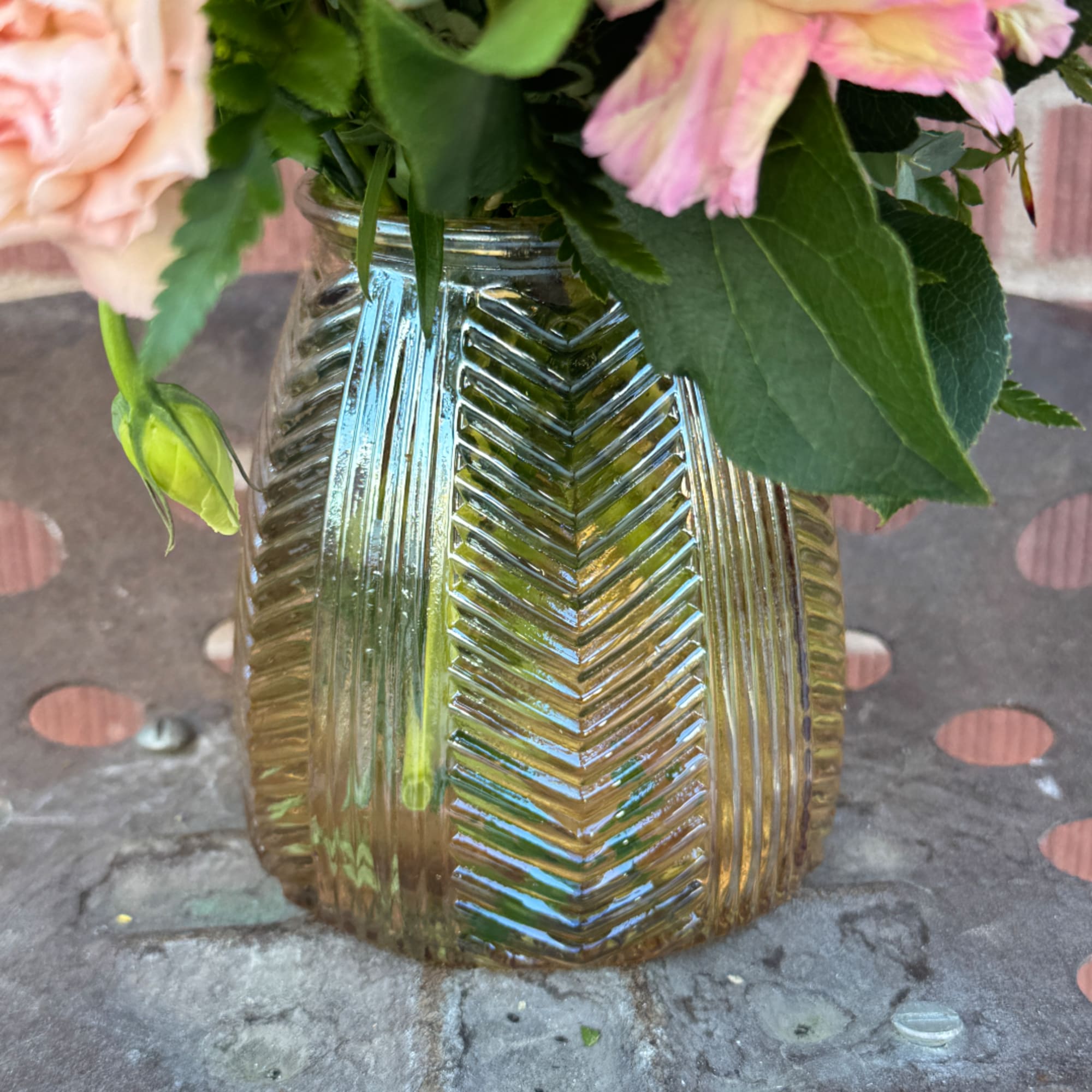 Pink flowers in a ribbed glass vase on a patterned surface