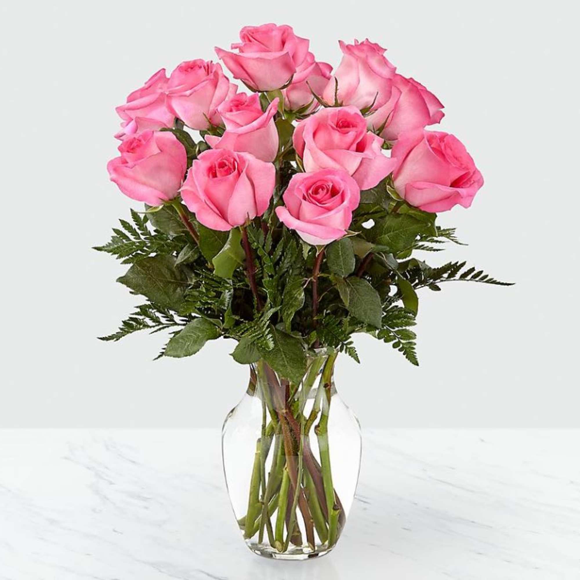 Dozen pink roses arranged in a clear glass vase on a light surface
