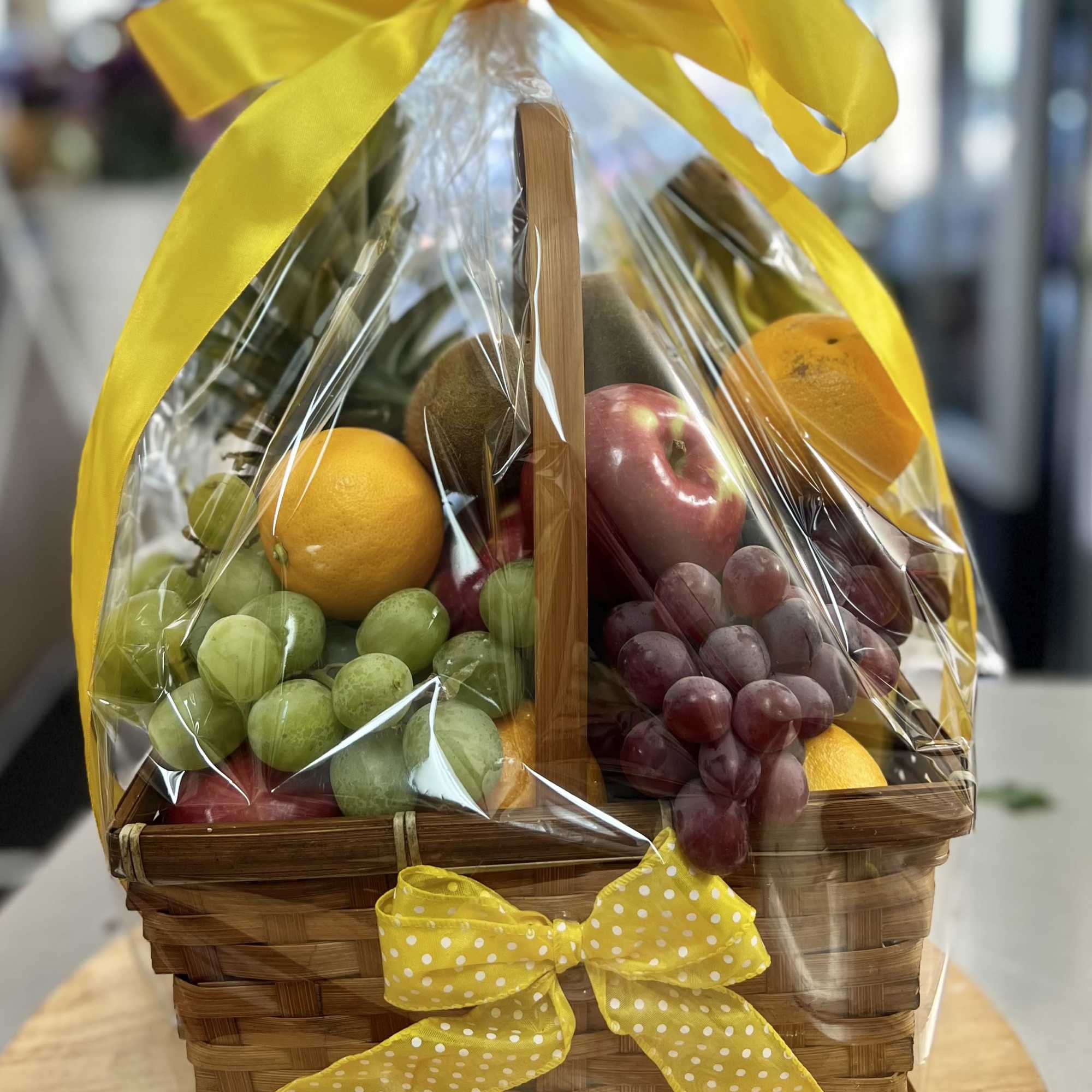 Fruit basket with grapes, oranges, apples, and kiwi wrapped in clear cellophane with yellow ribbon