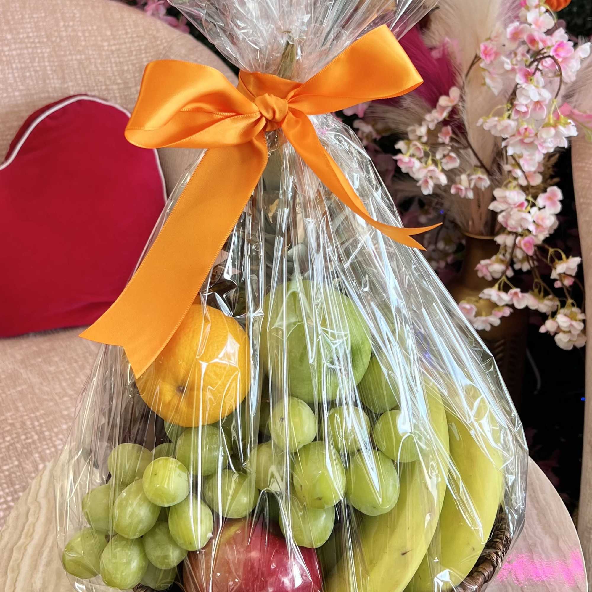 Fruit basket wrapped in clear plastic with an orange ribbon