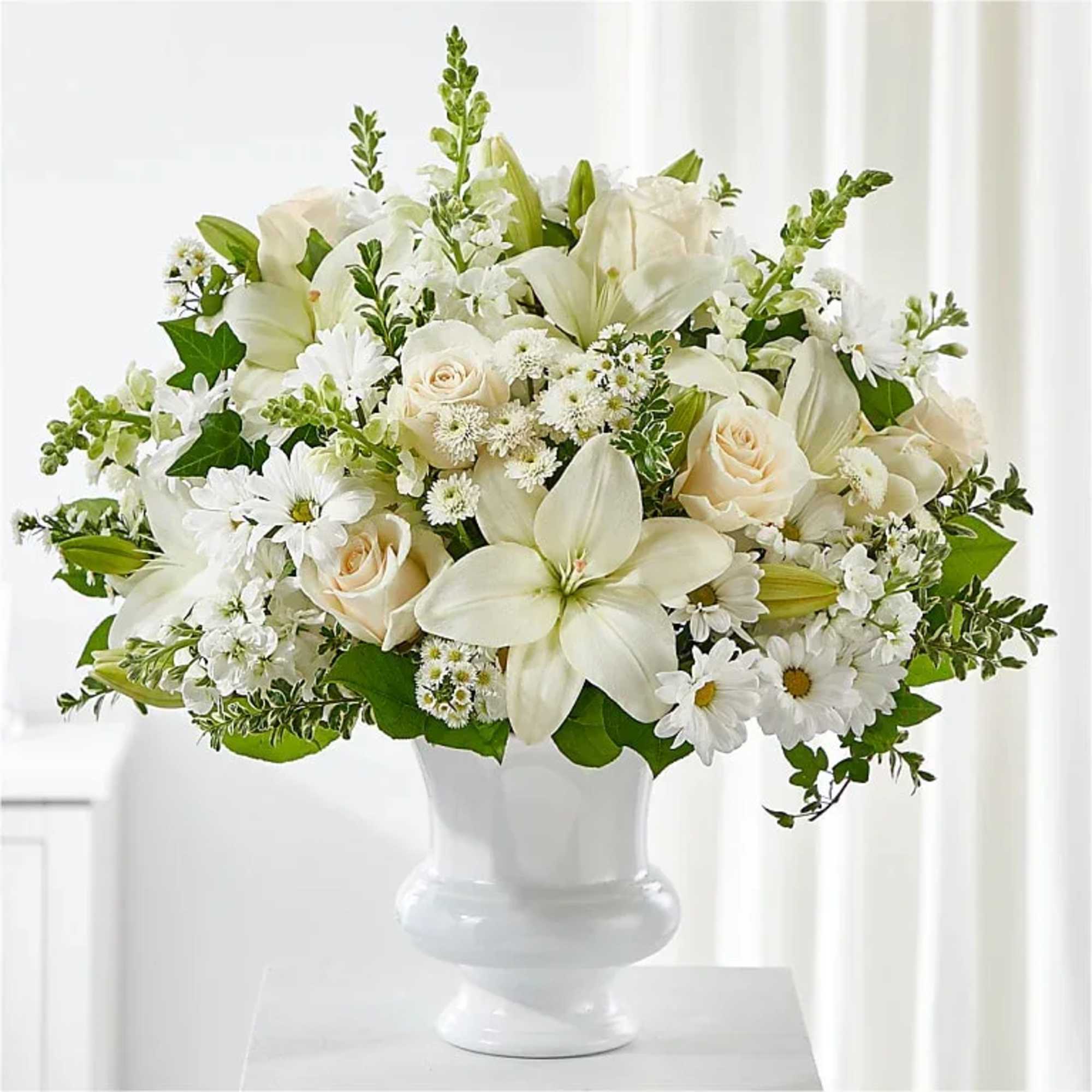 White lilies, roses, and daisies arranged in a white vase