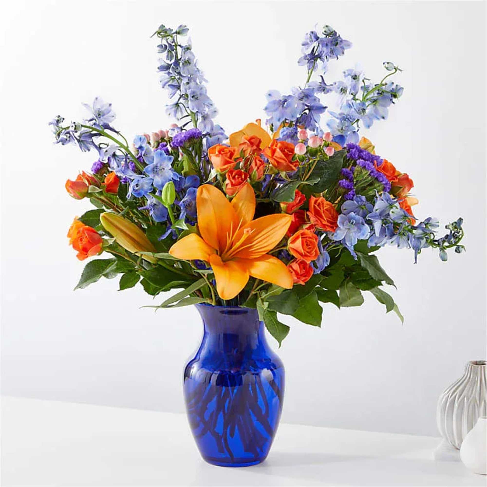 Orange lilies and blue flowers in a cobalt vase