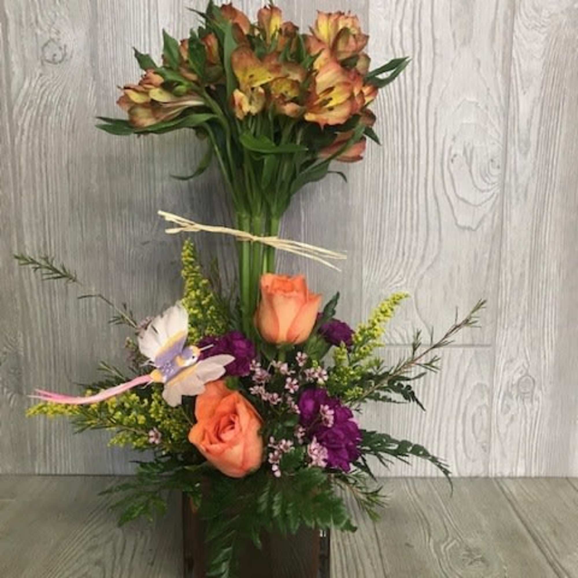 Tall mixed arrangement with orange roses, purple flowers, and alstroemeria in a brown glass cube vase