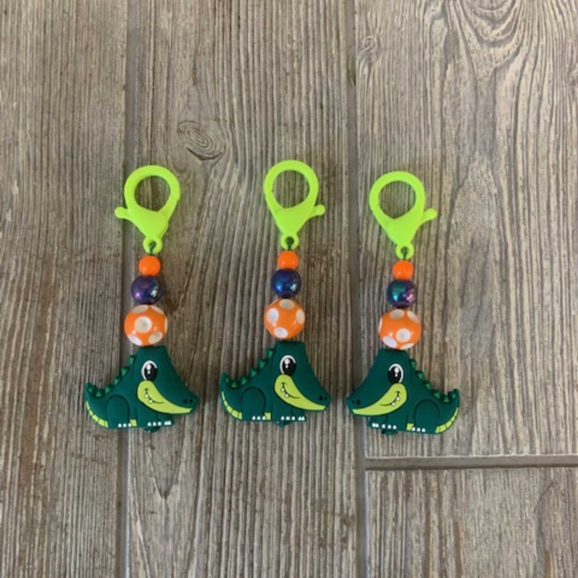 Three colorful crocodile-shaped clip charms on a wood surface