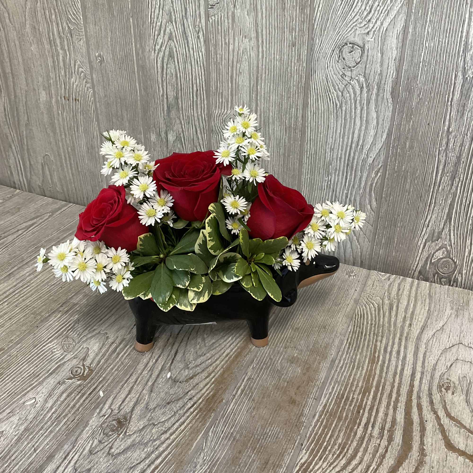 Red roses and white daisies arranged in a black cow-shaped container