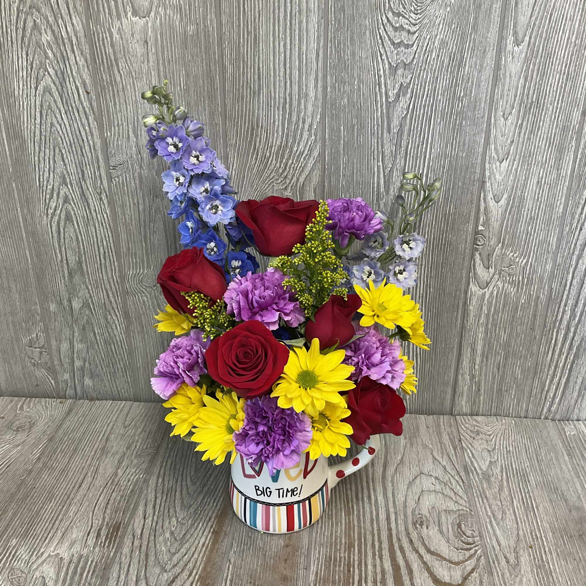 Colorful bouquet in a striped mug with roses, daisies, and purple blooms