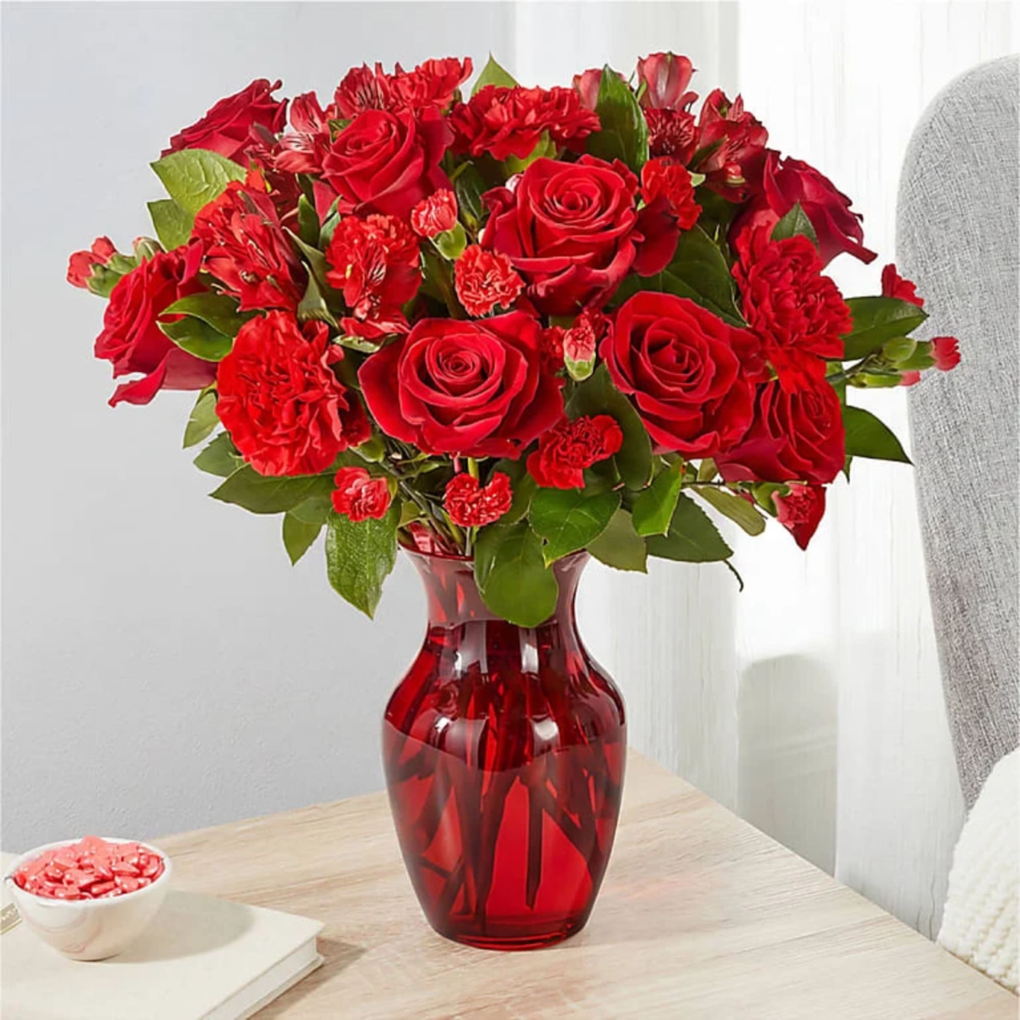 Red roses and carnations in a red glass vase on a table