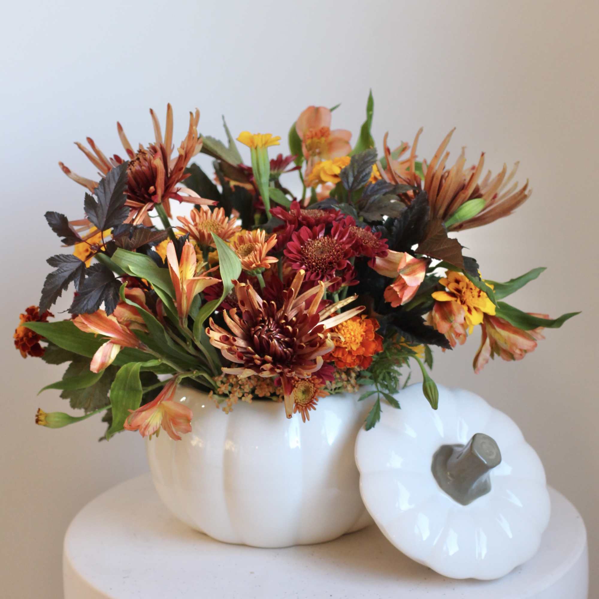Autumn flower arrangement in a white pumpkin-shaped vase with a lid beside it