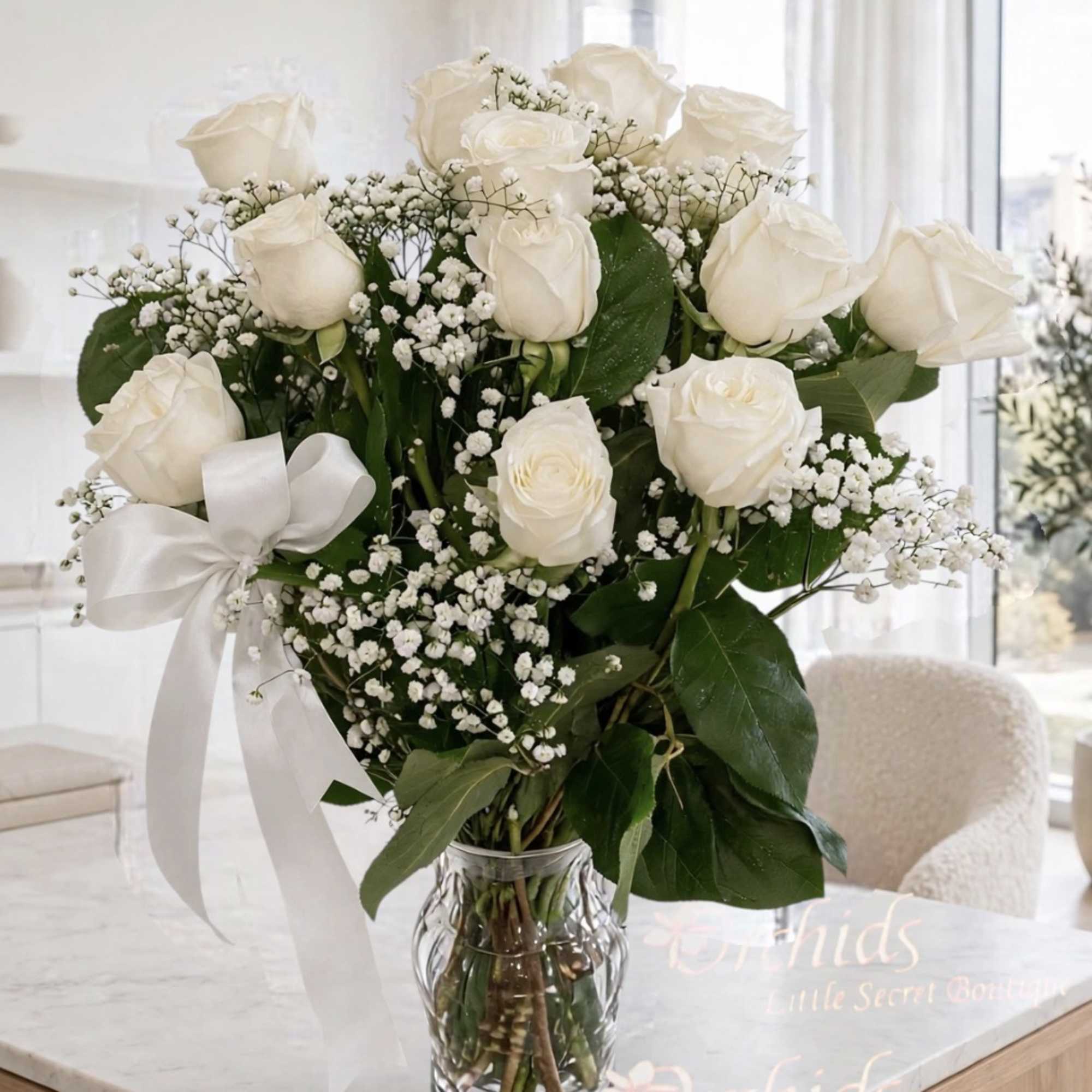 White rose bouquet with baby's breath in a clear glass vase and white ribbon