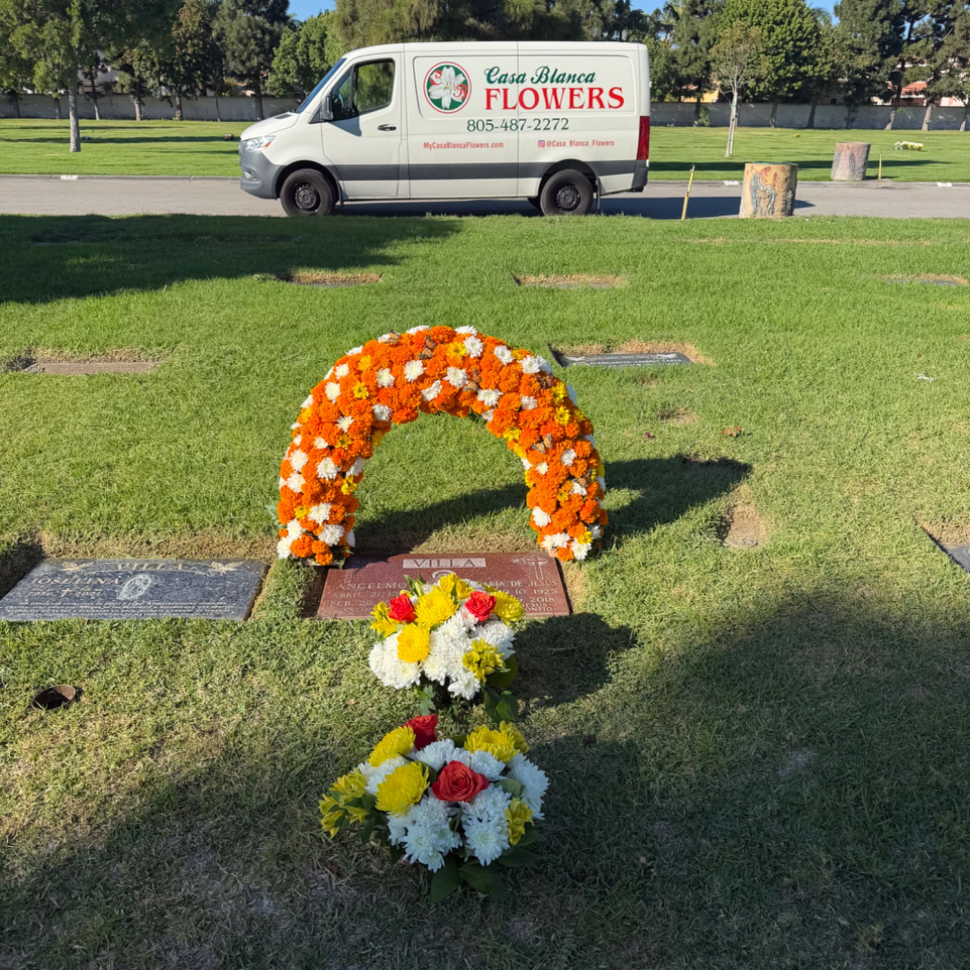 Orange and white floral wreath with two small bouquets on a gravesite