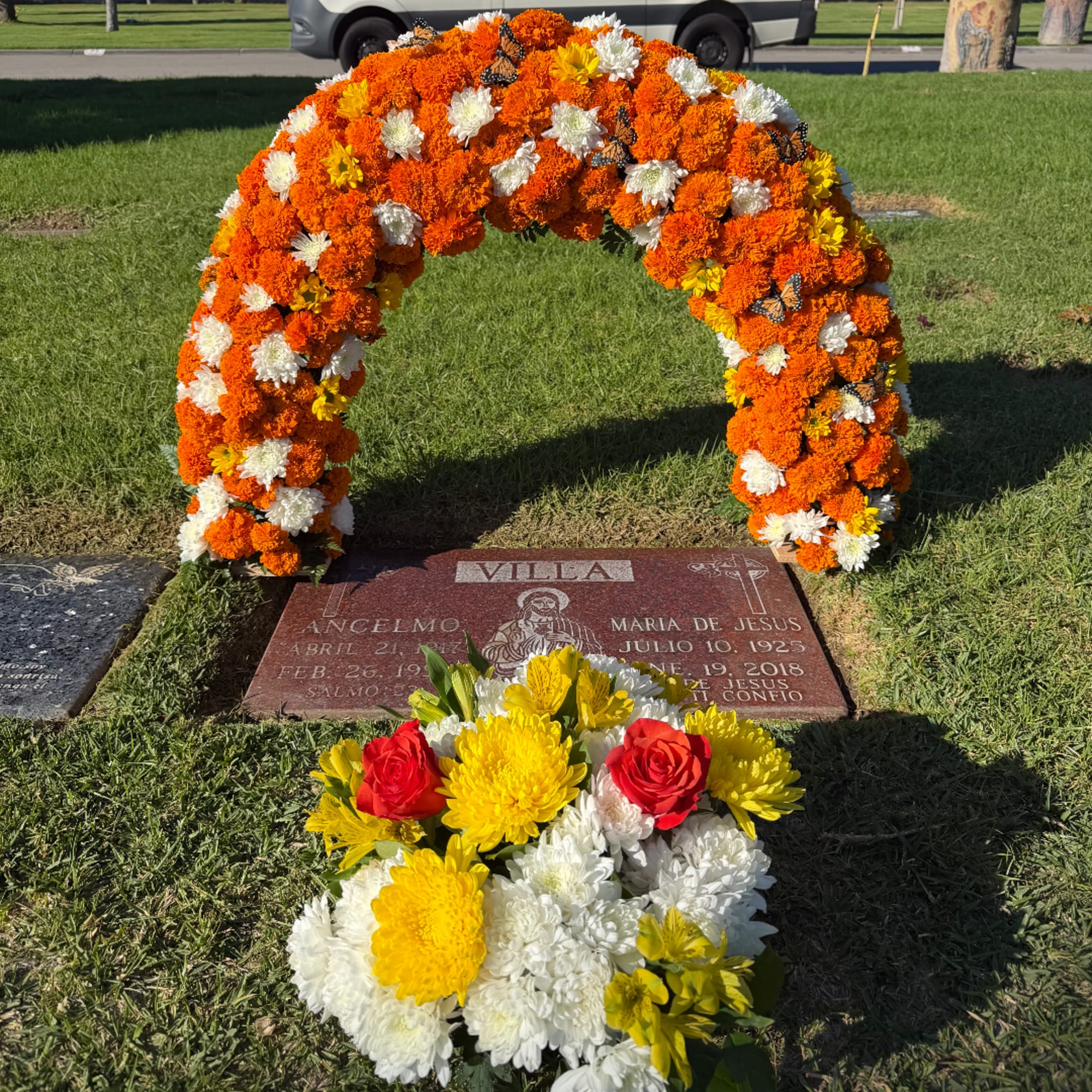 Orange and white floral arch over a grave with a mixed bouquet in front