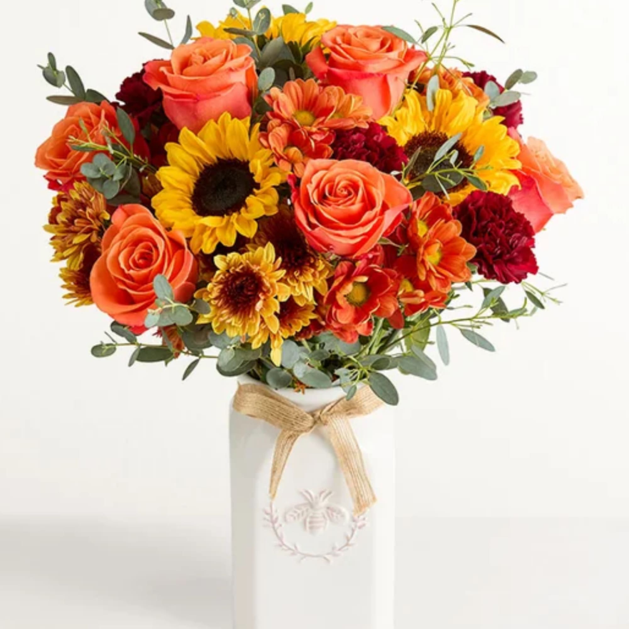 Orange roses and yellow sunflowers in a white vase with a ribbon