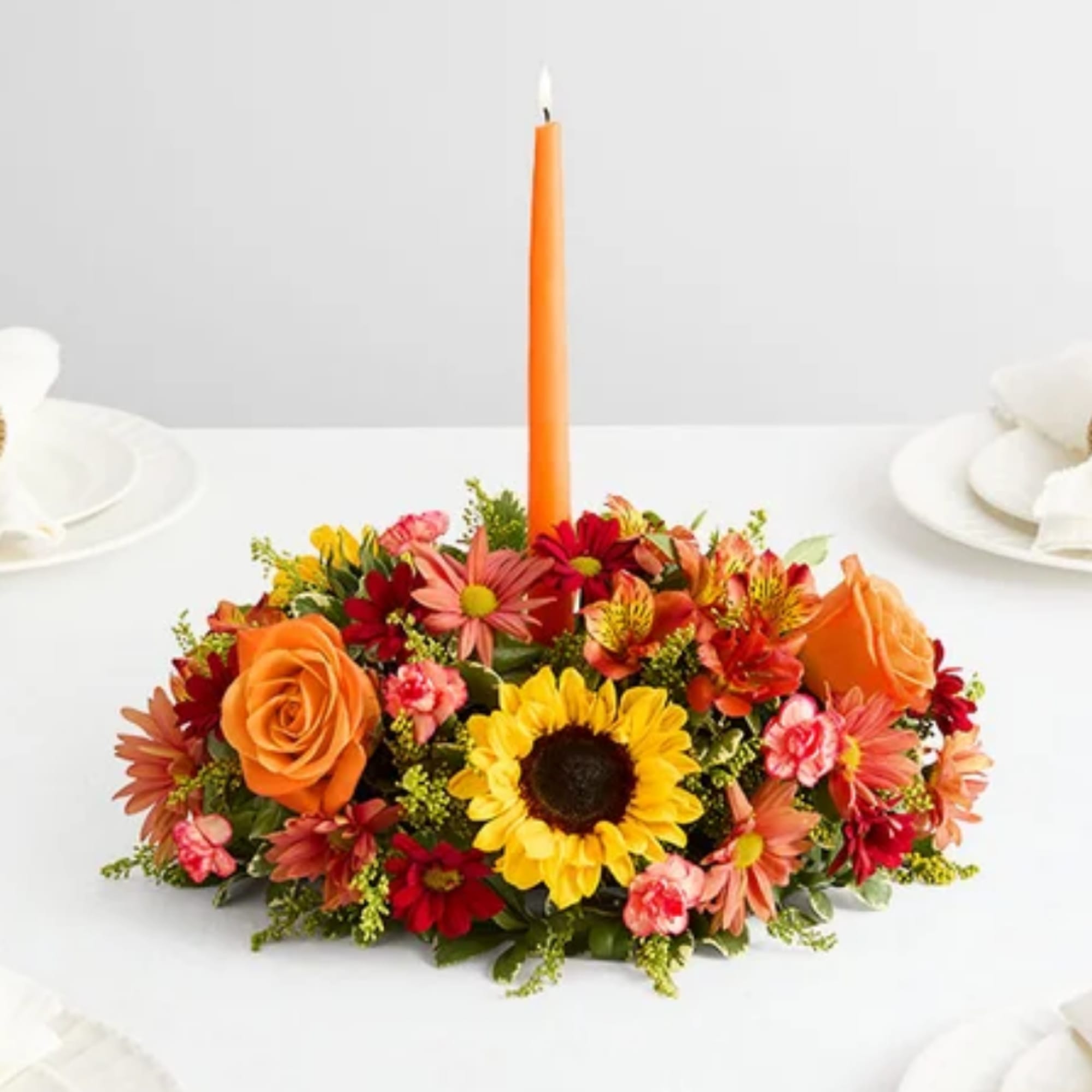 Orange candle in a low floral centerpiece with sunflowers and roses