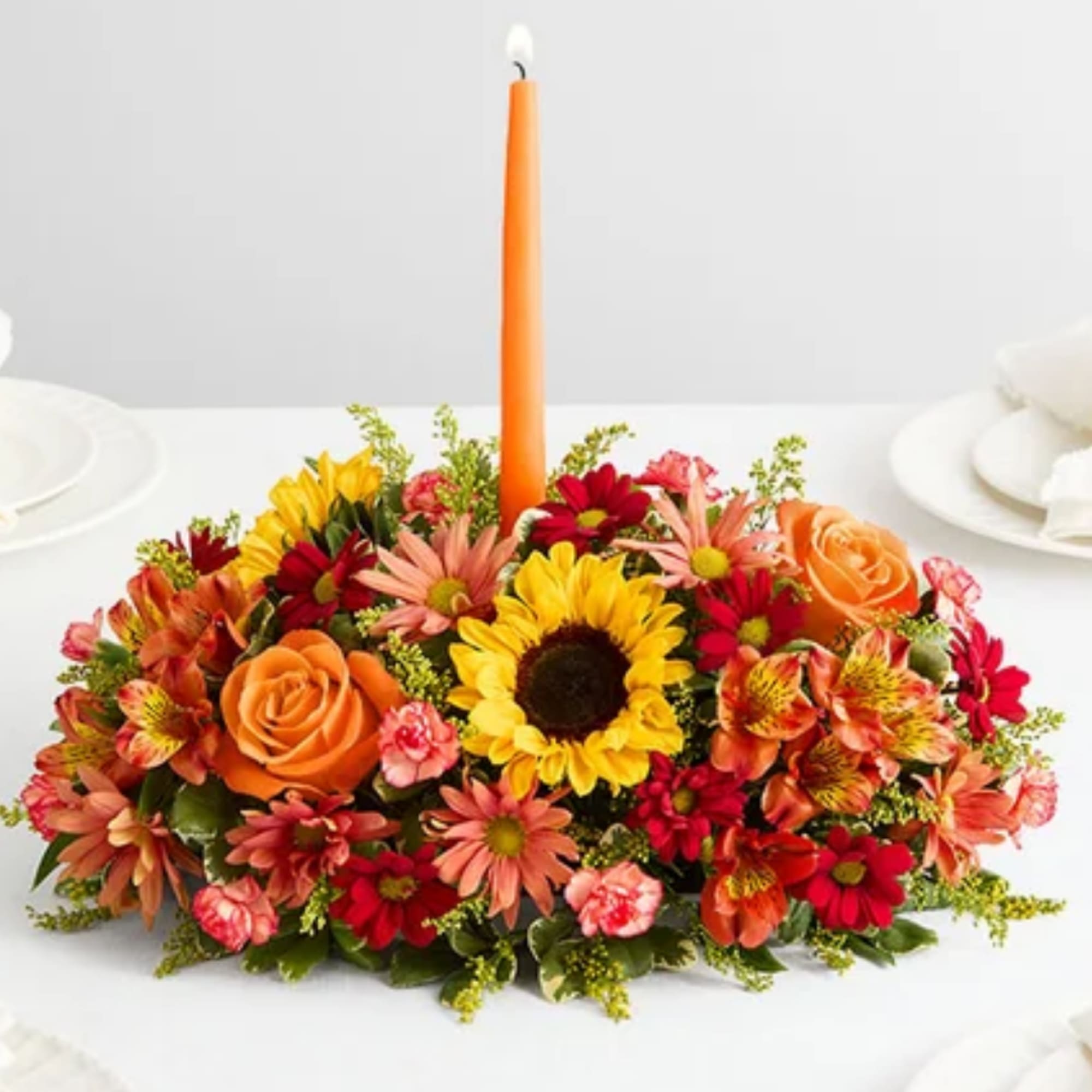 Low floral centerpiece with a tall orange candle in the middle