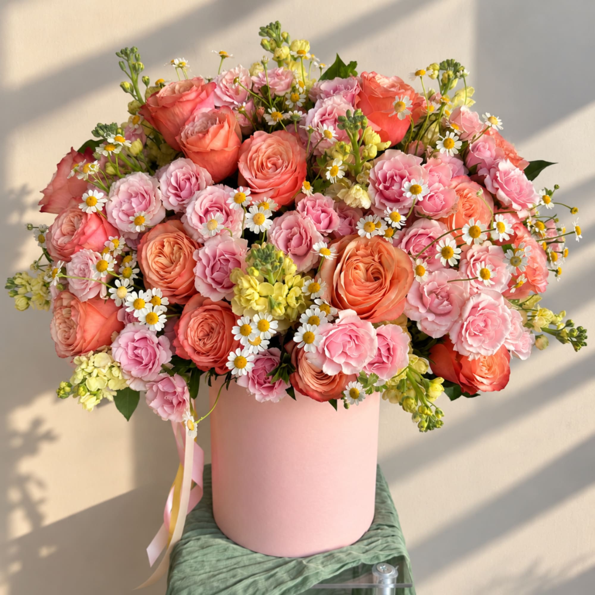 Pink and coral roses with small white daisies in a pink hatbox