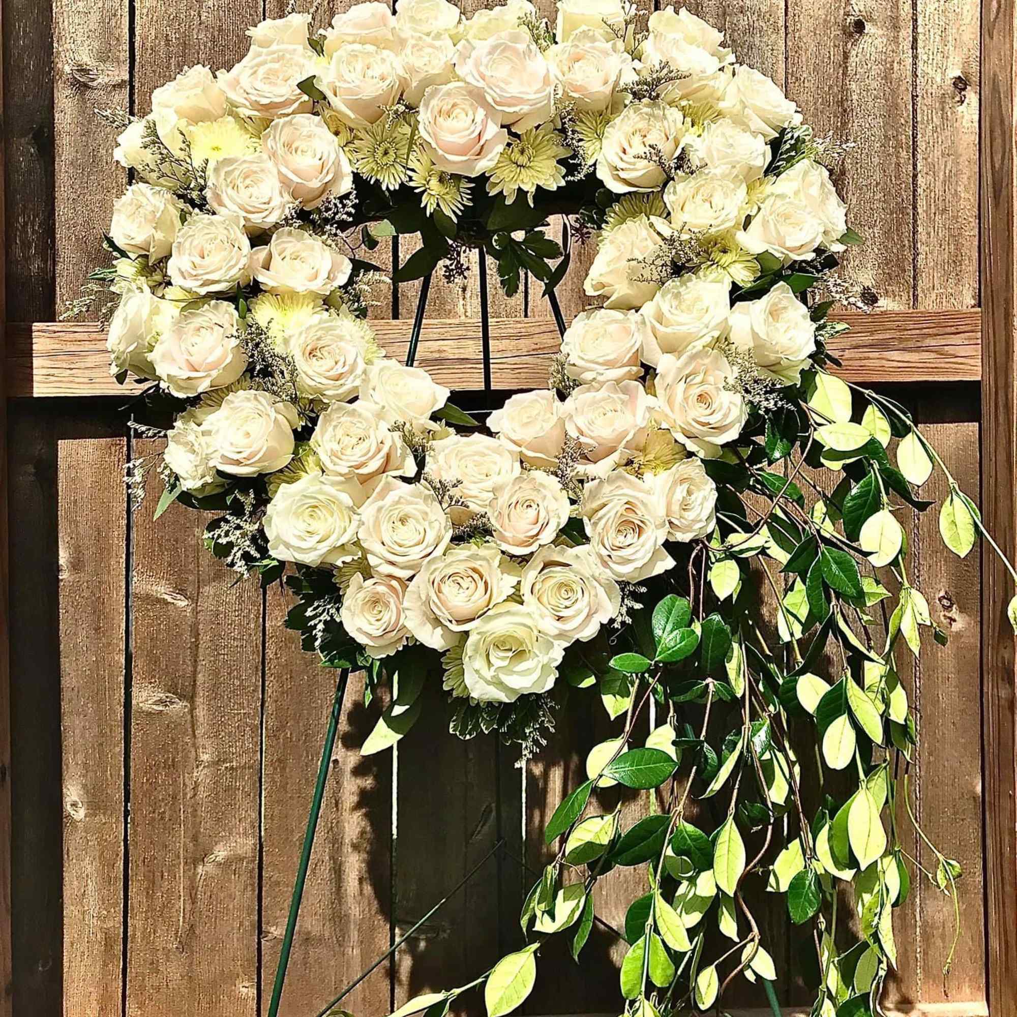 Heart-shaped standing wreath of ivory roses with trailing greenery on one side