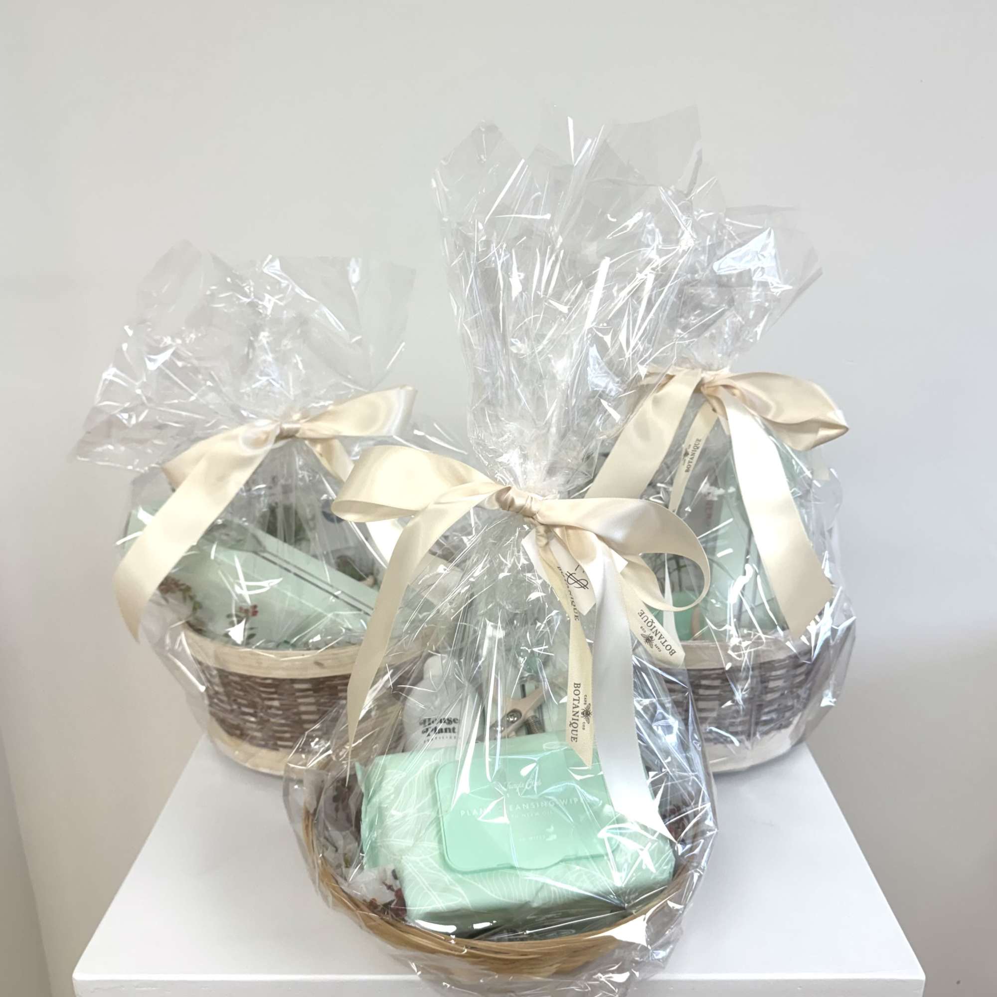 Three wrapped gift baskets with cream ribbons on a white surface
