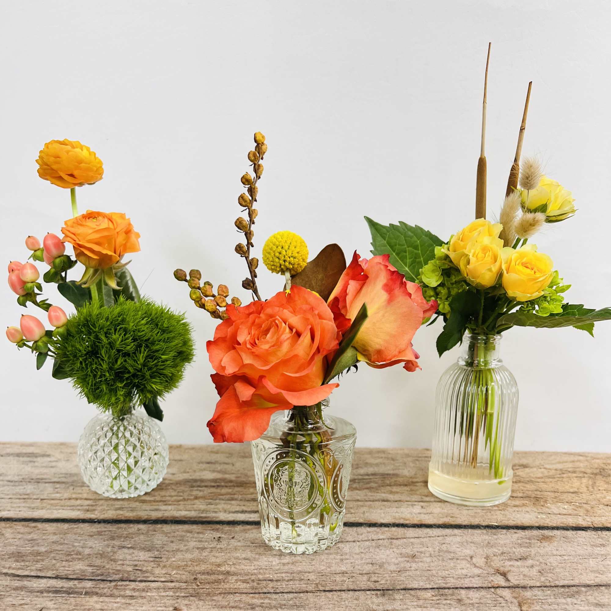 Three small floral arrangements in glass vases on a wooden surface, photo 2 of 3