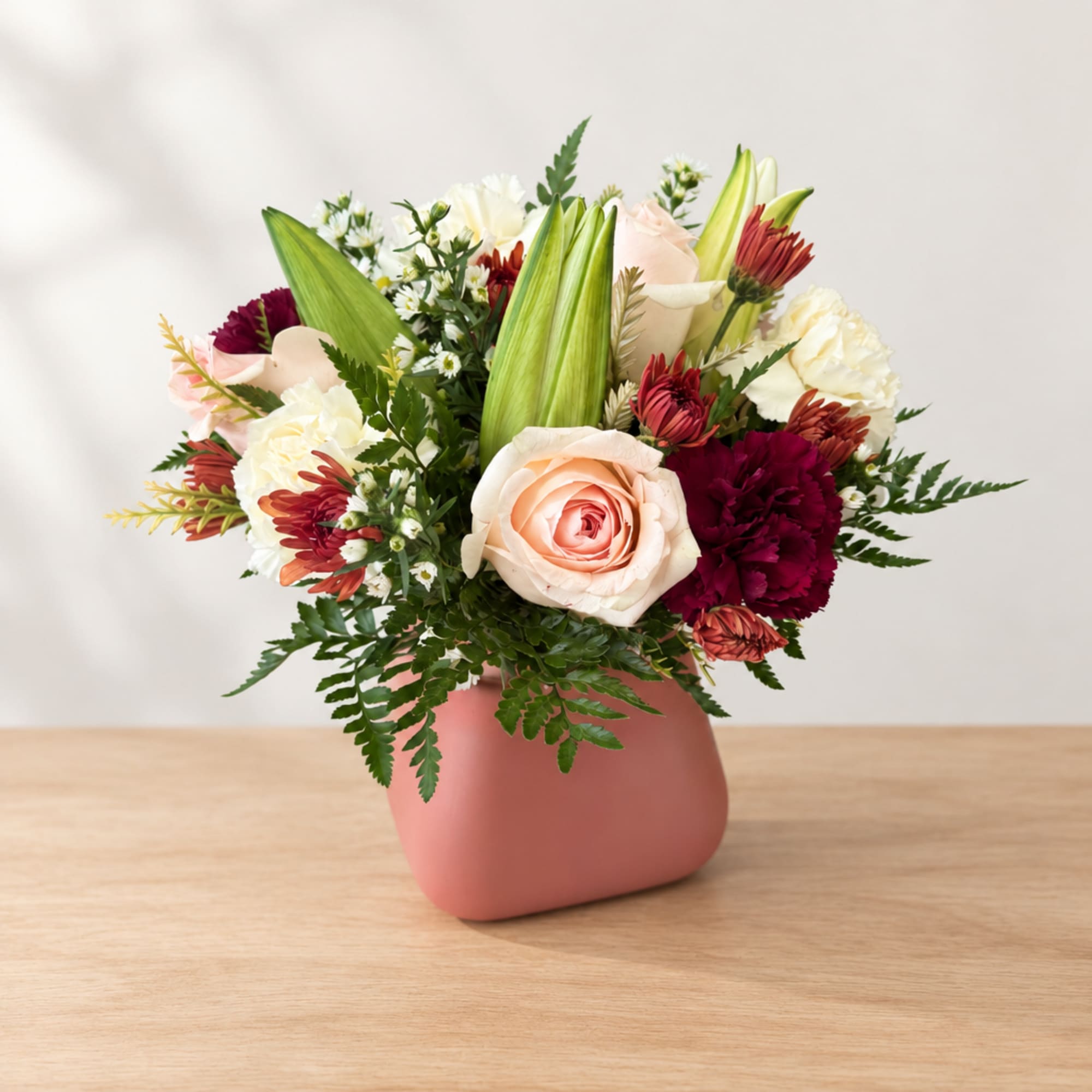 Mixed bouquet of roses, carnations, and lilies in a pink vase