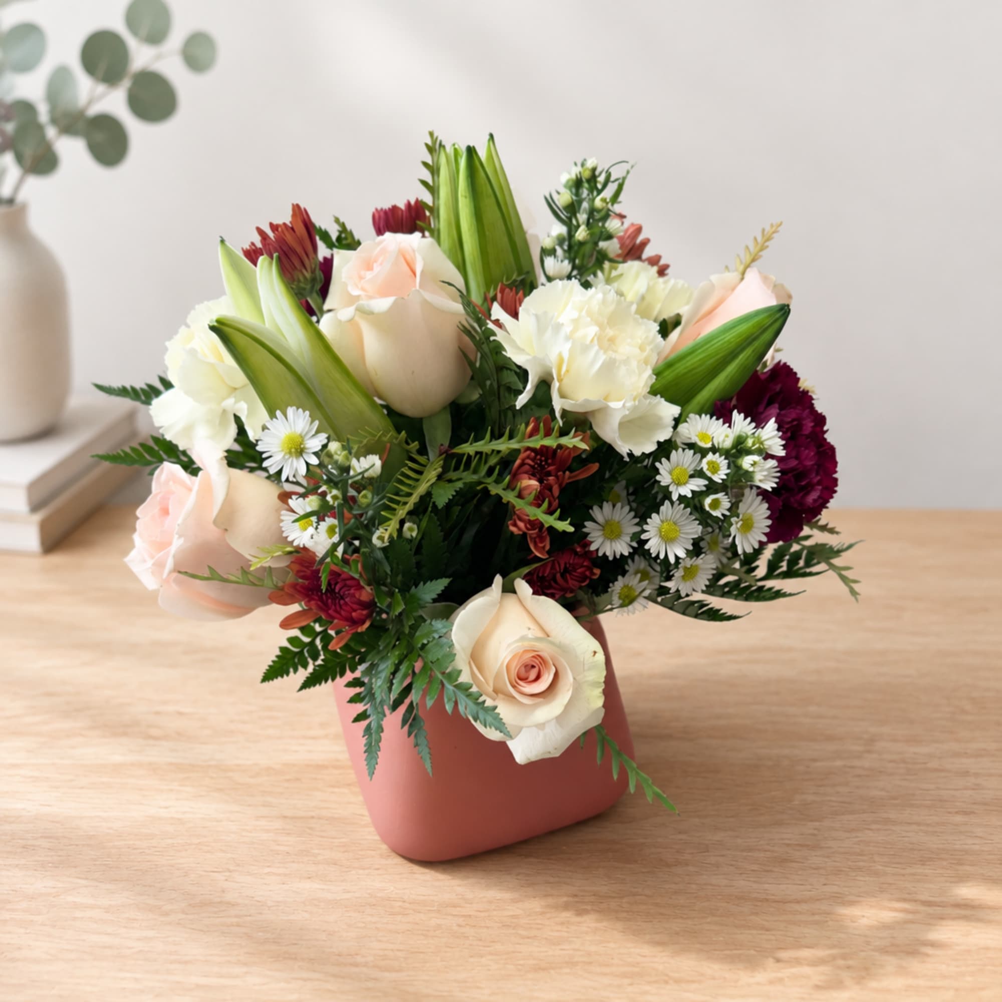 Mixed bouquet of roses, lilies, and daisies in a pink vase