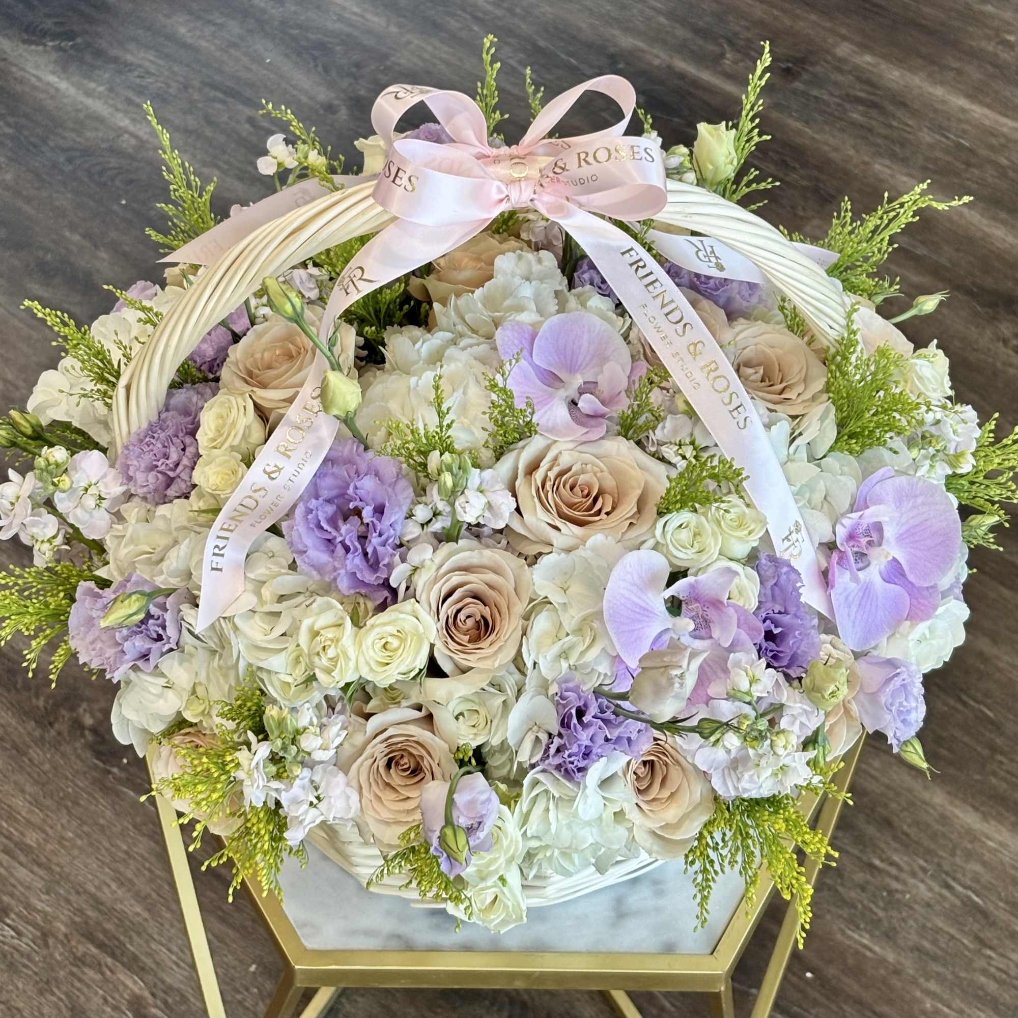 Pastel flower basket with roses, orchids, and lavender blooms tied with a pink ribbon