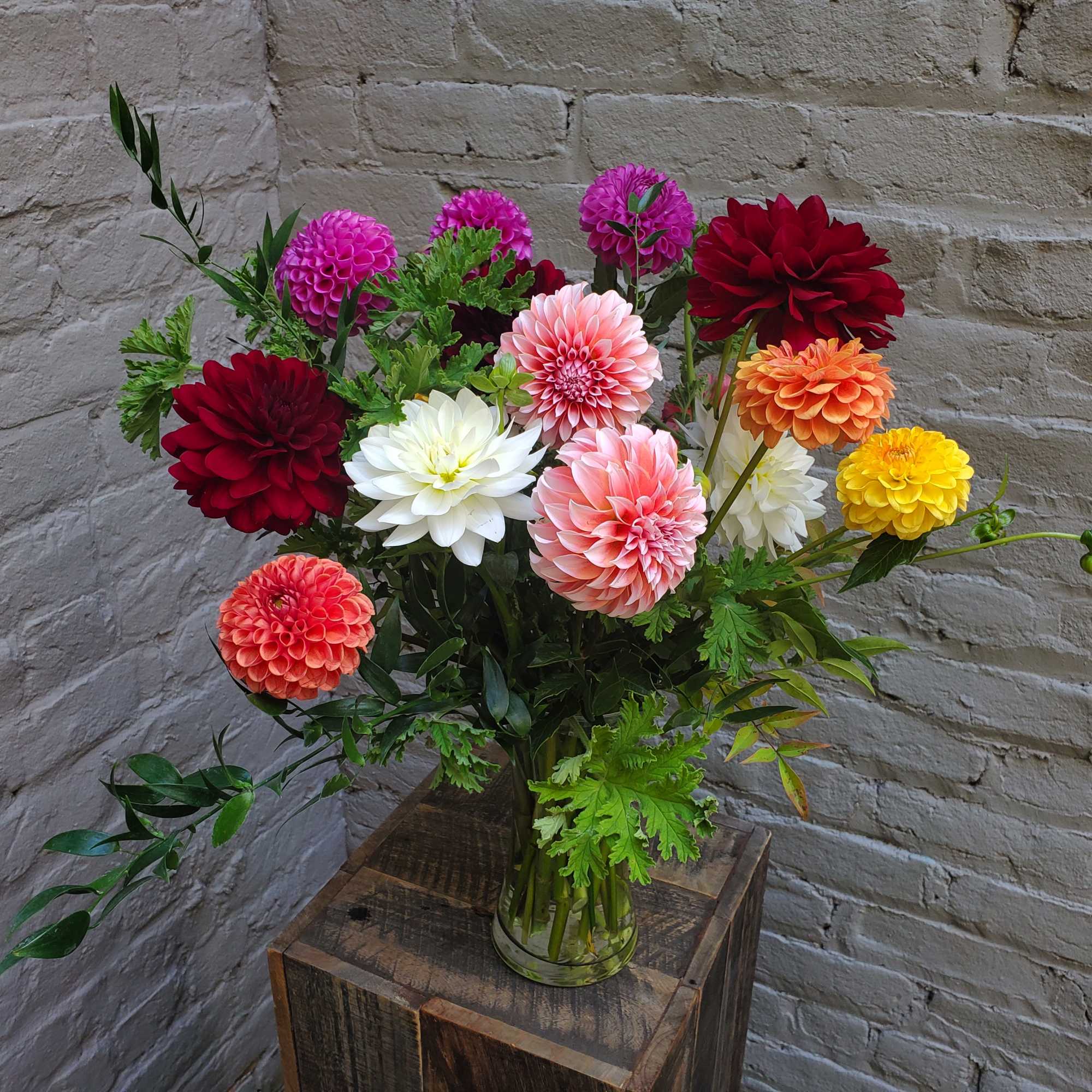 Mixed dahlias in a glass vase on a wooden stand