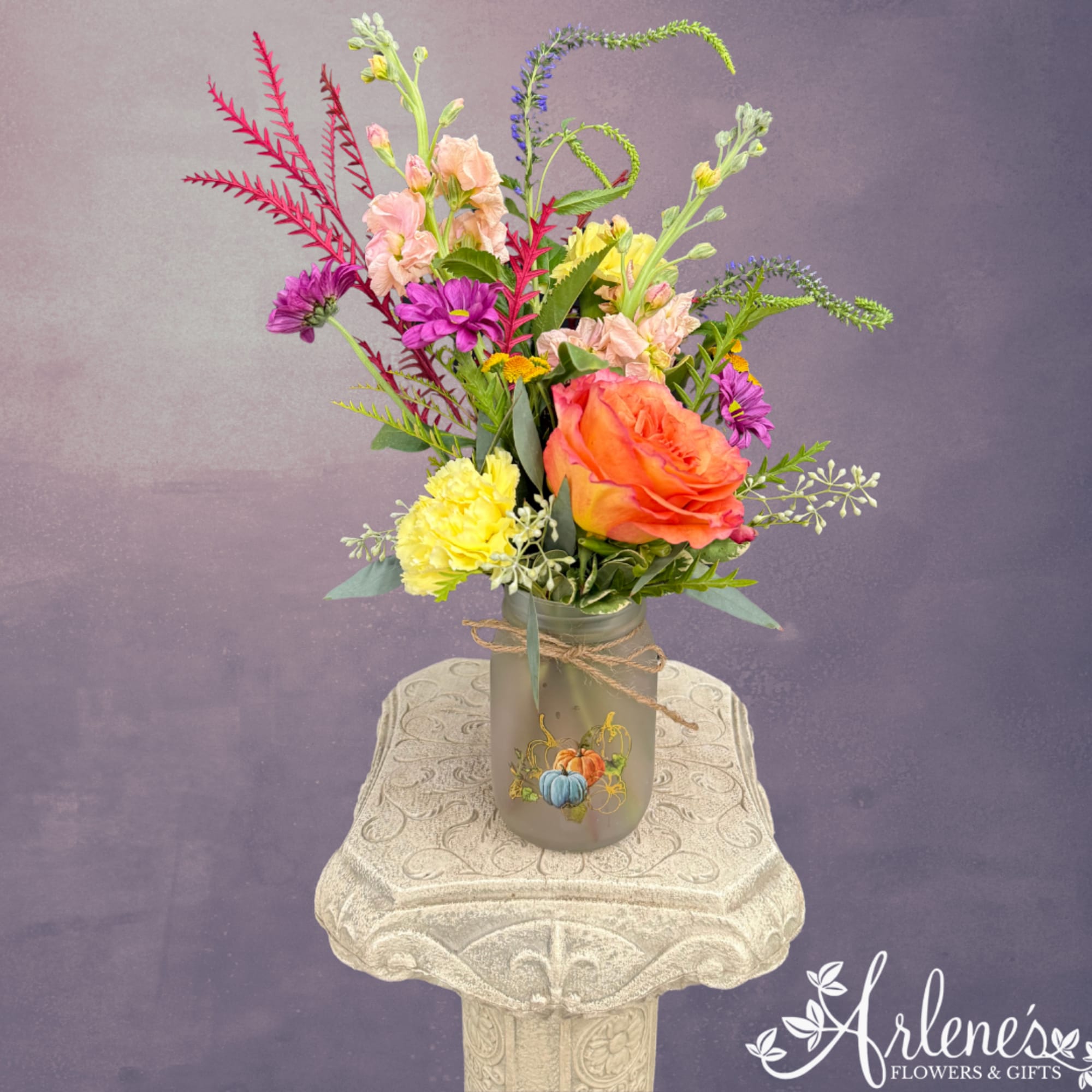 Mixed bouquet in a frosted jar vase with orange, pink, purple, and yellow flowers