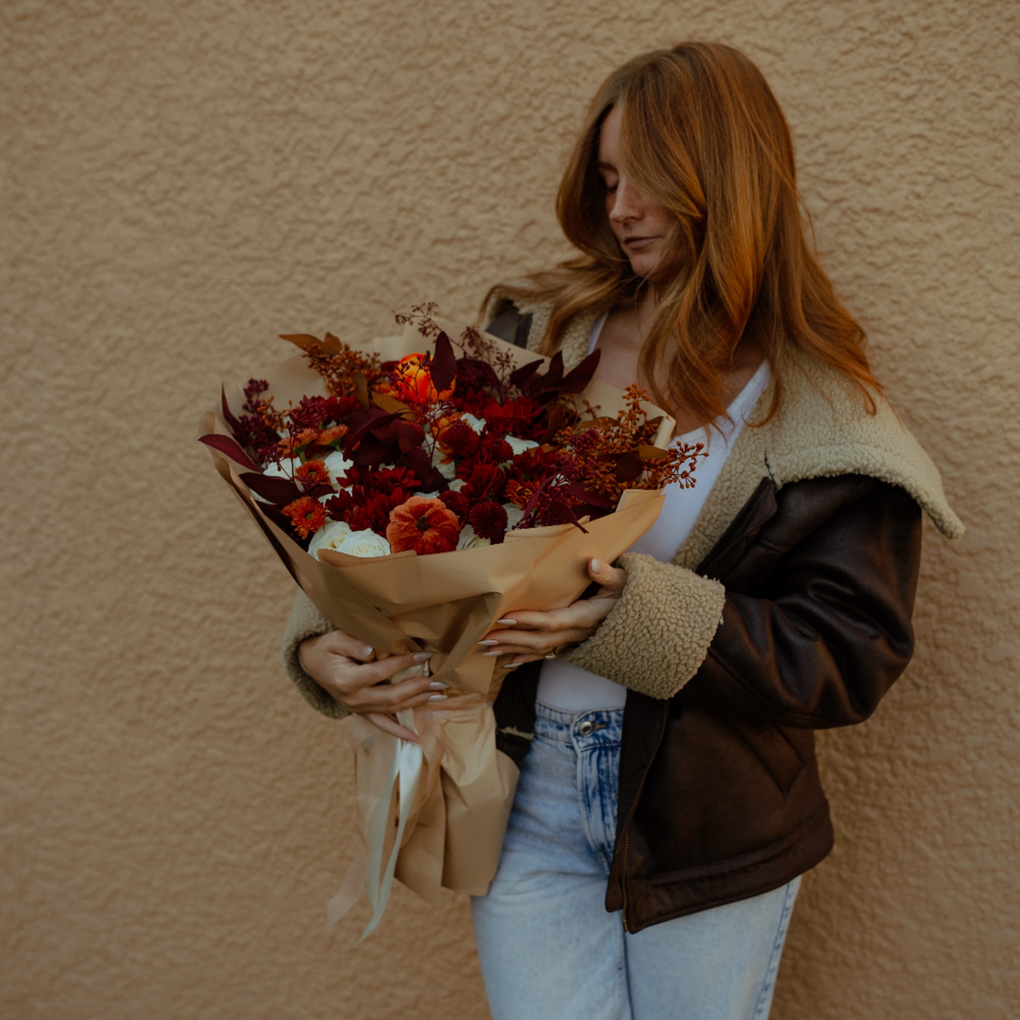Woman holding a bouquet of red and orange flowers wrapped in tan paper