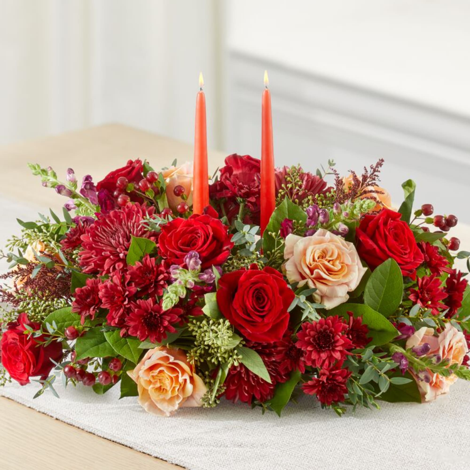 Red and peach roses with burgundy blooms and two orange candles