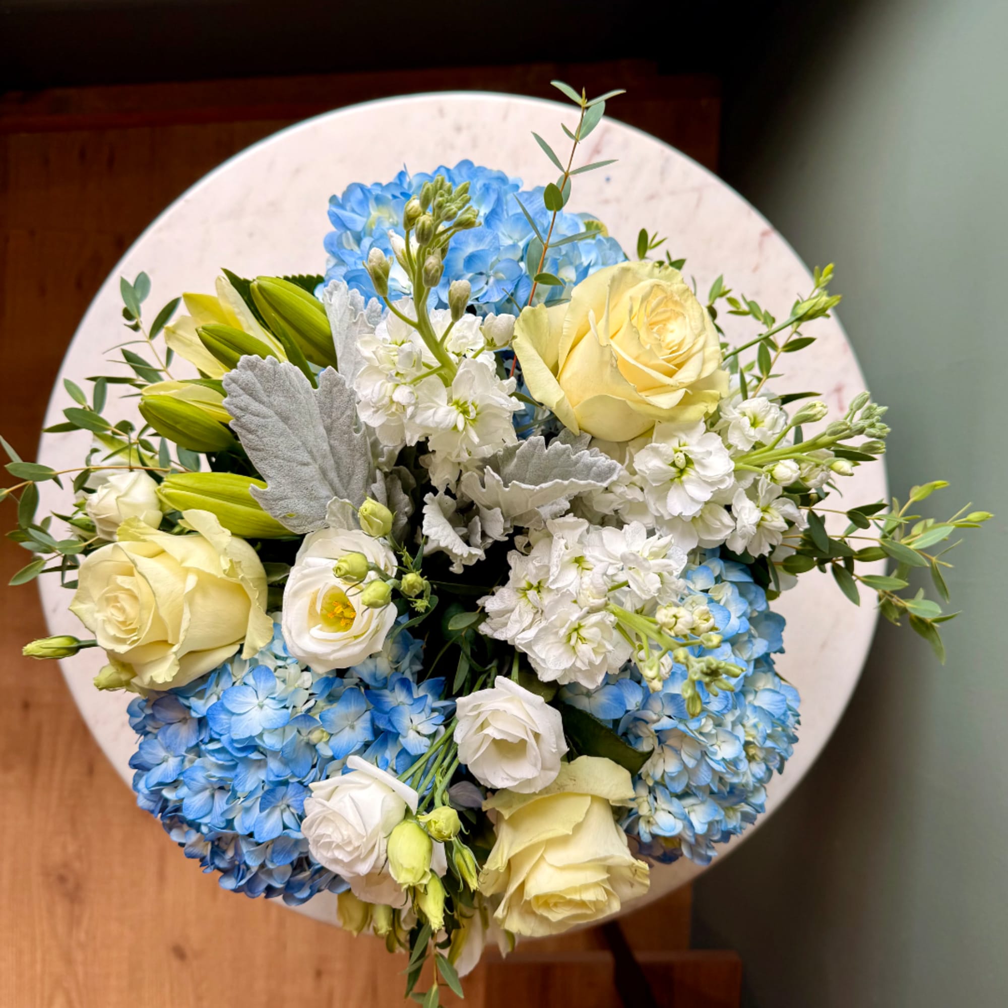 Bouquet of blue hydrangeas, cream roses, and white blooms in a round arrangement