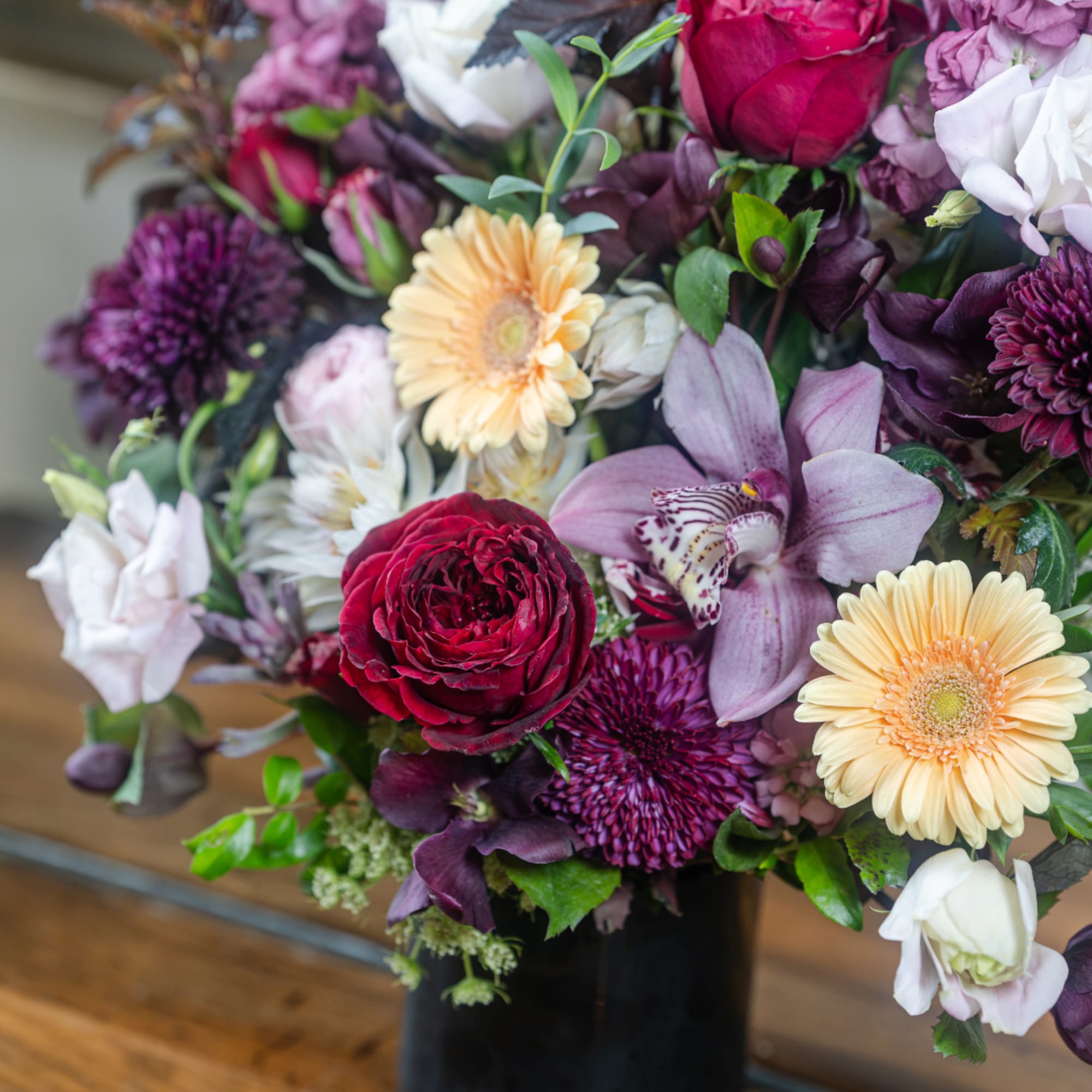 Mixed bouquet with burgundy, lavender, and cream flowers in a black vase