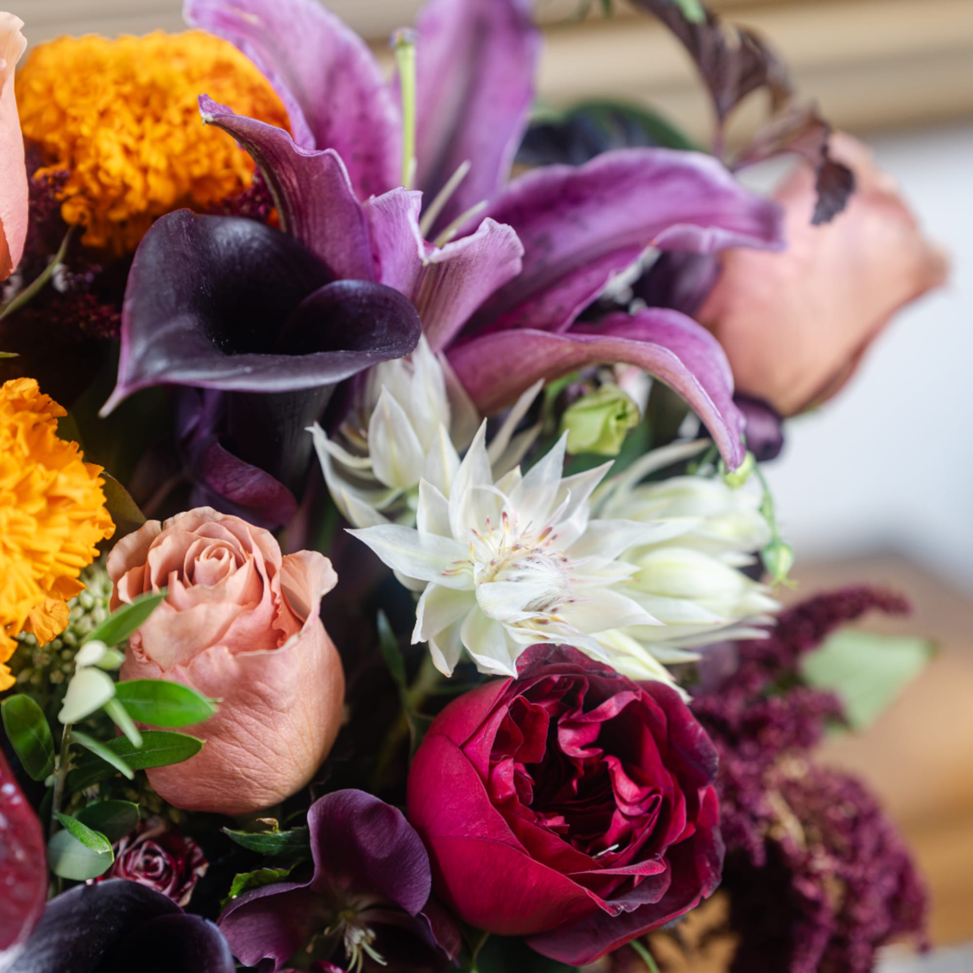 Close-up bouquet with purple lilies, roses, and orange marigolds