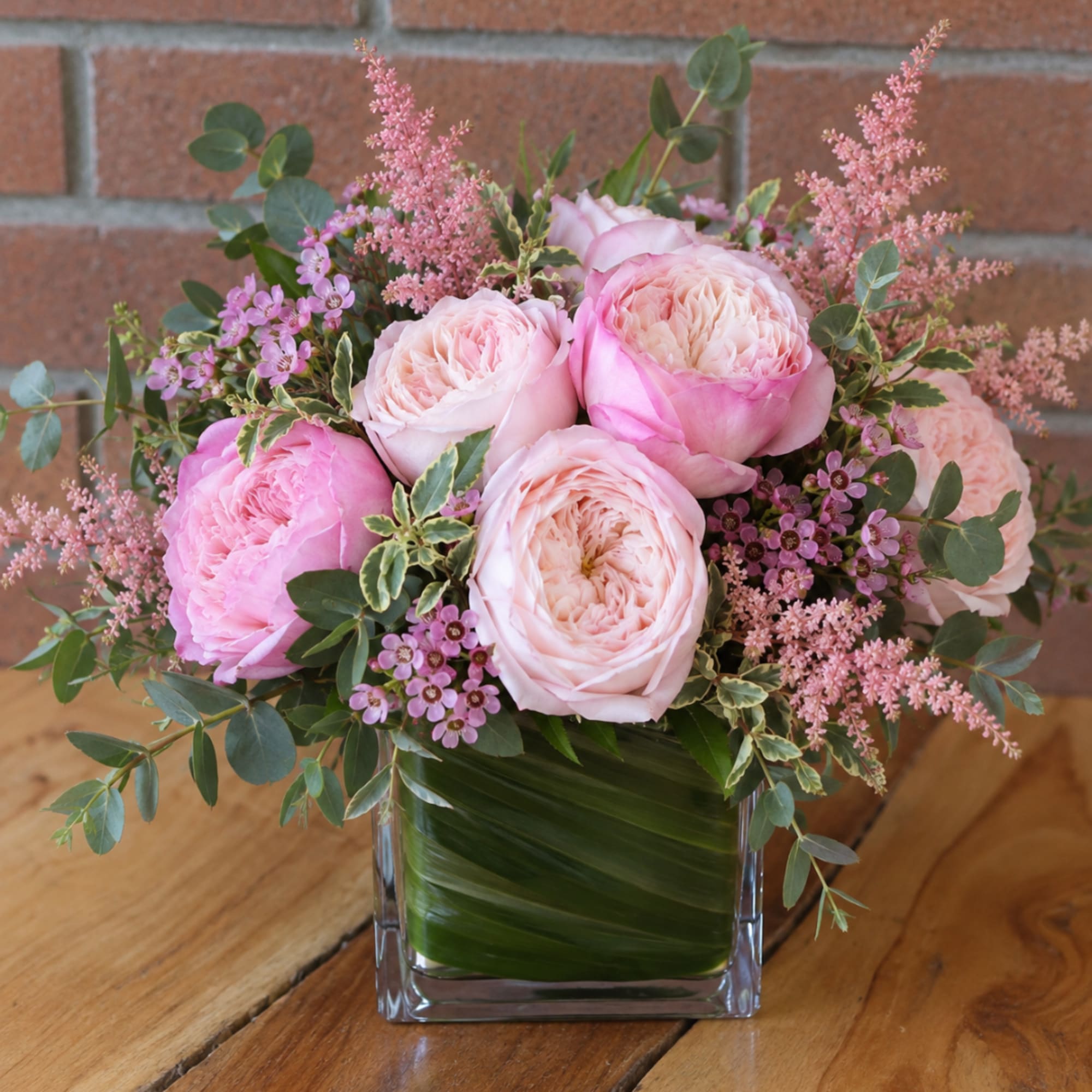 Pink roses and small purple flowers in a clear square vase.