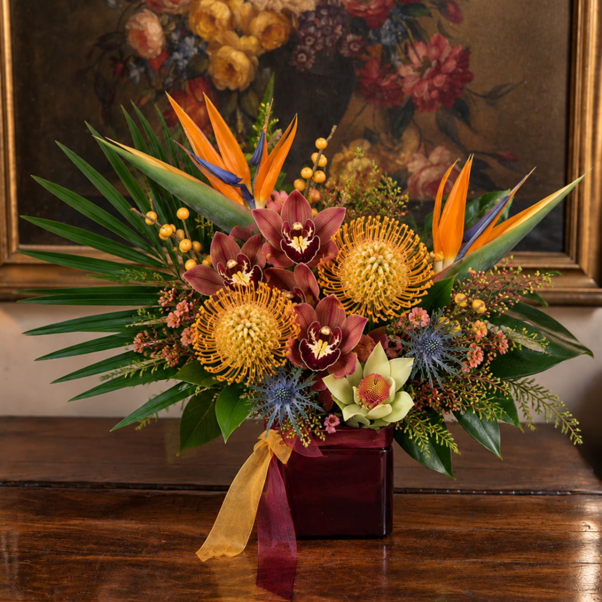 Tropical flower arrangement in a burgundy vase with orange and burgundy blooms