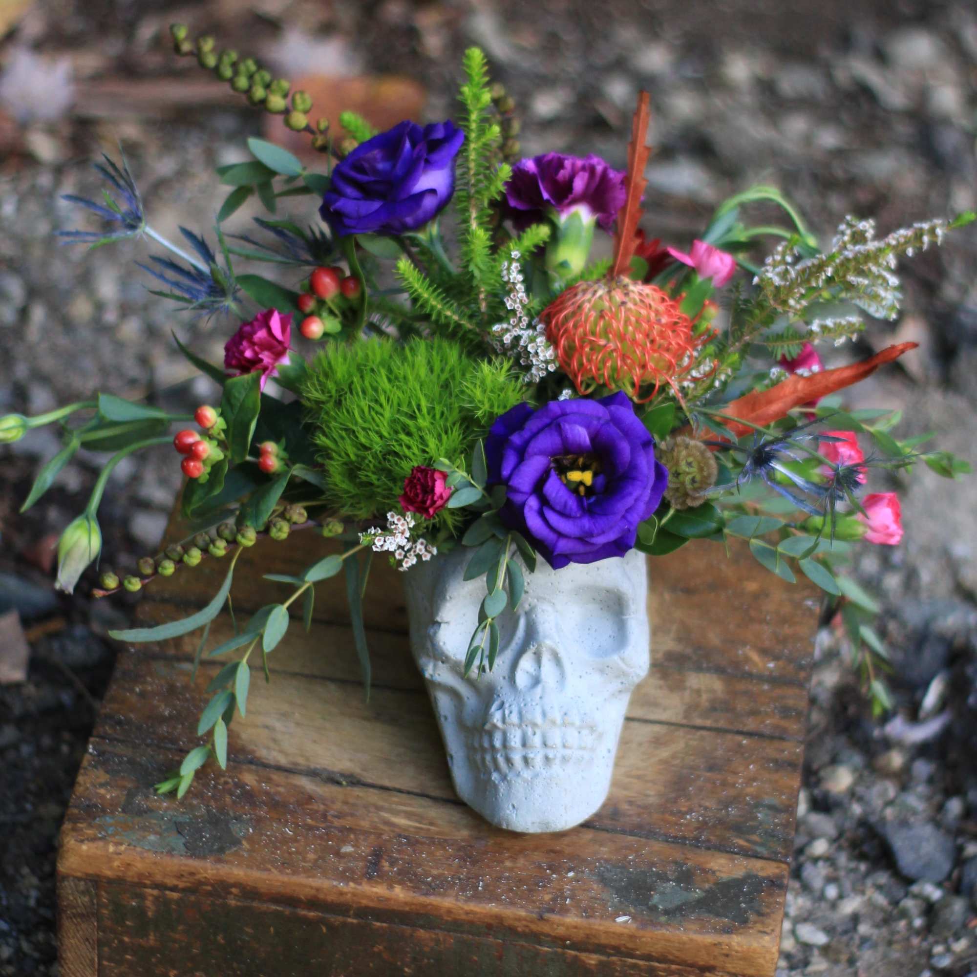 Colorful bouquet in a white skull vase with purple blooms and orange accents