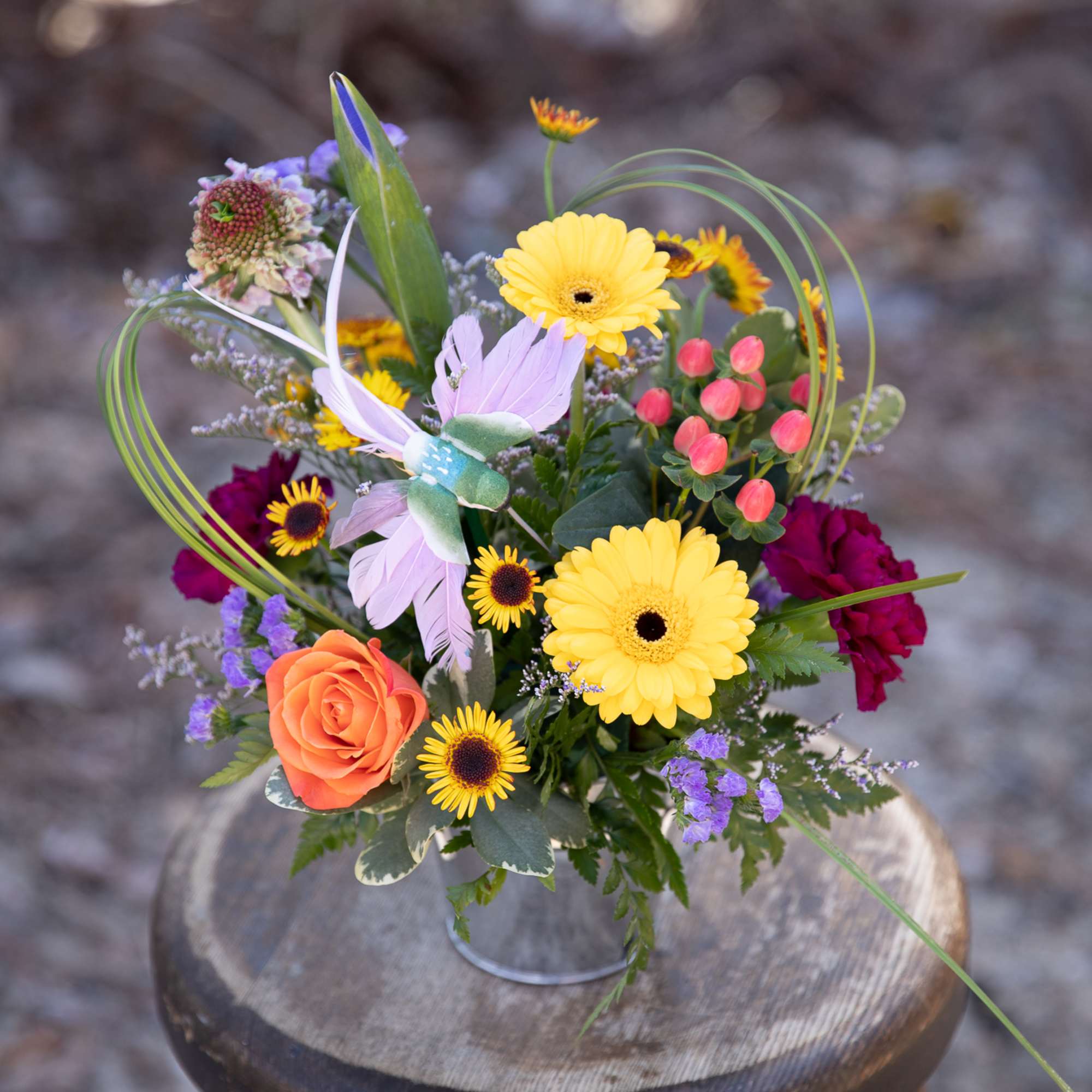 Mixed bouquet with yellow daisies, orange rose, and purple accents in a metal container