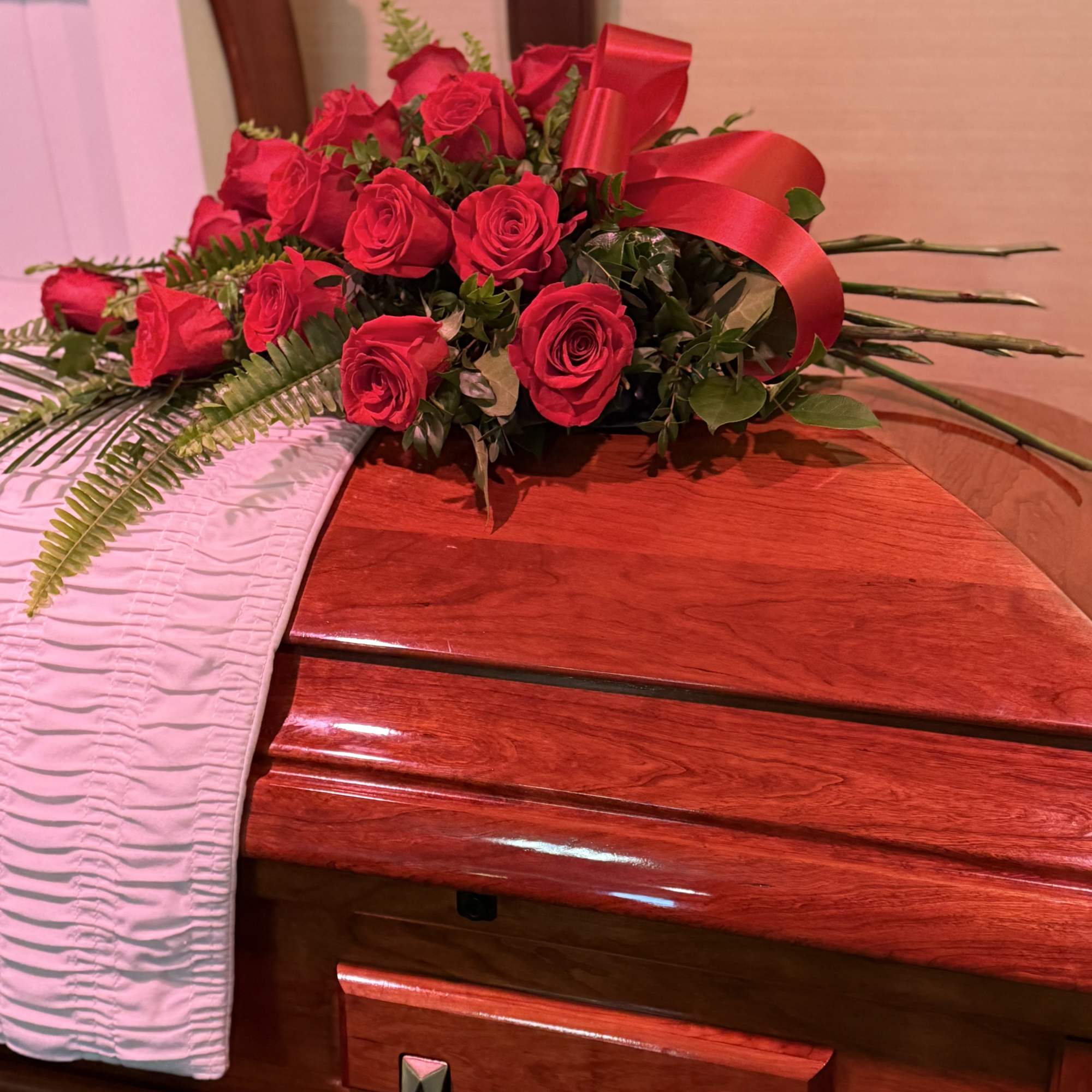 Red rose arrangement with a satin ribbon on a polished wooden casket