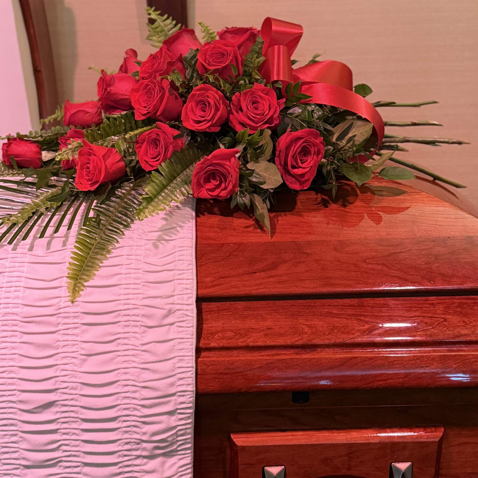 Red rose casket spray with ribbon and fern accents